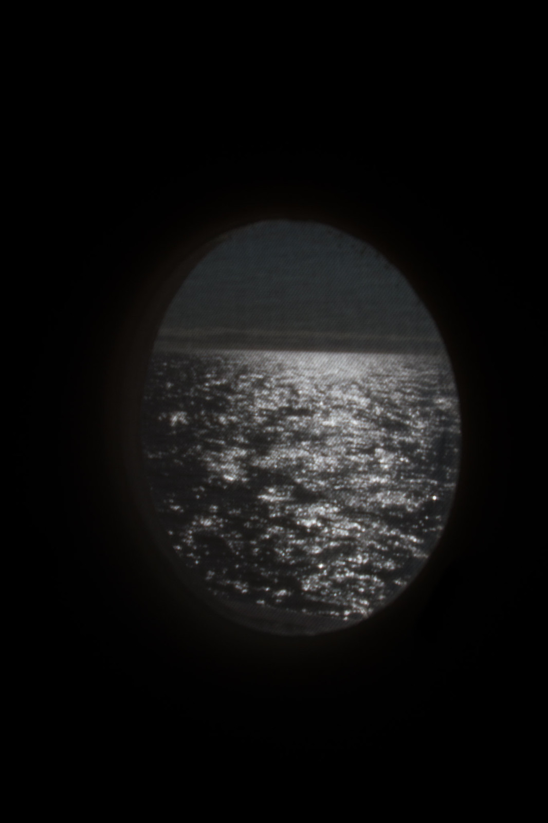Moonlight shimmering on the ocean, seen through a dark oval cruise-ship porthole.