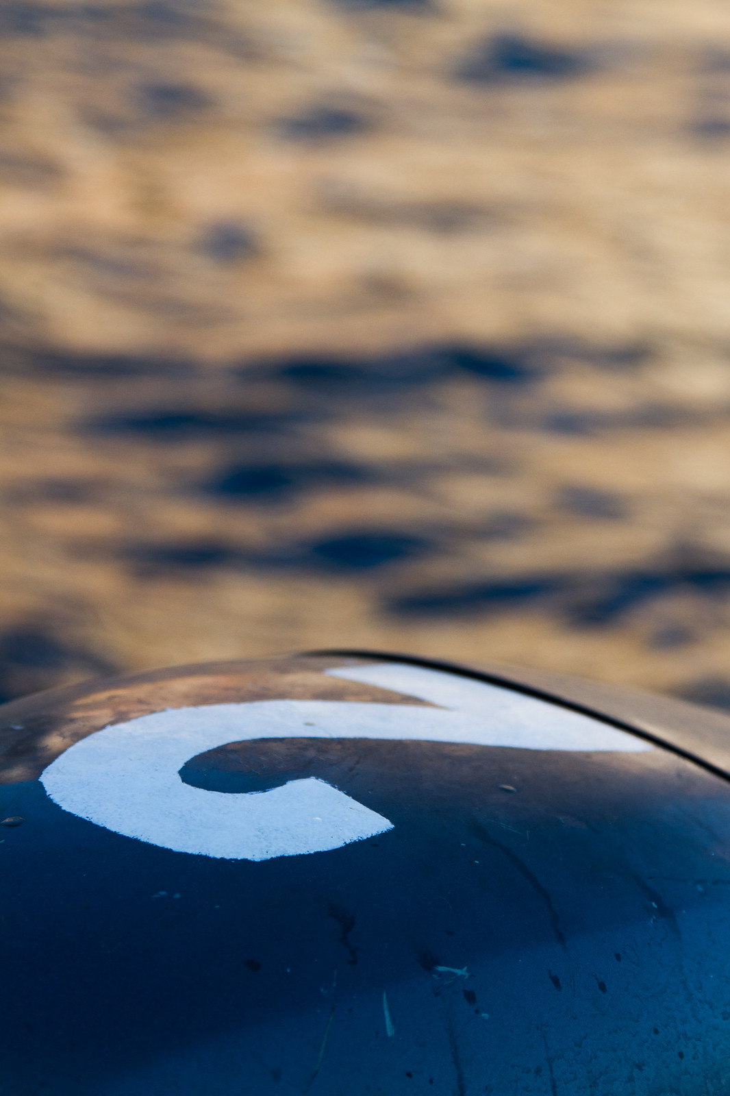 White number "2" hand-painted on a curved dark blue buoy floating on rippling water.