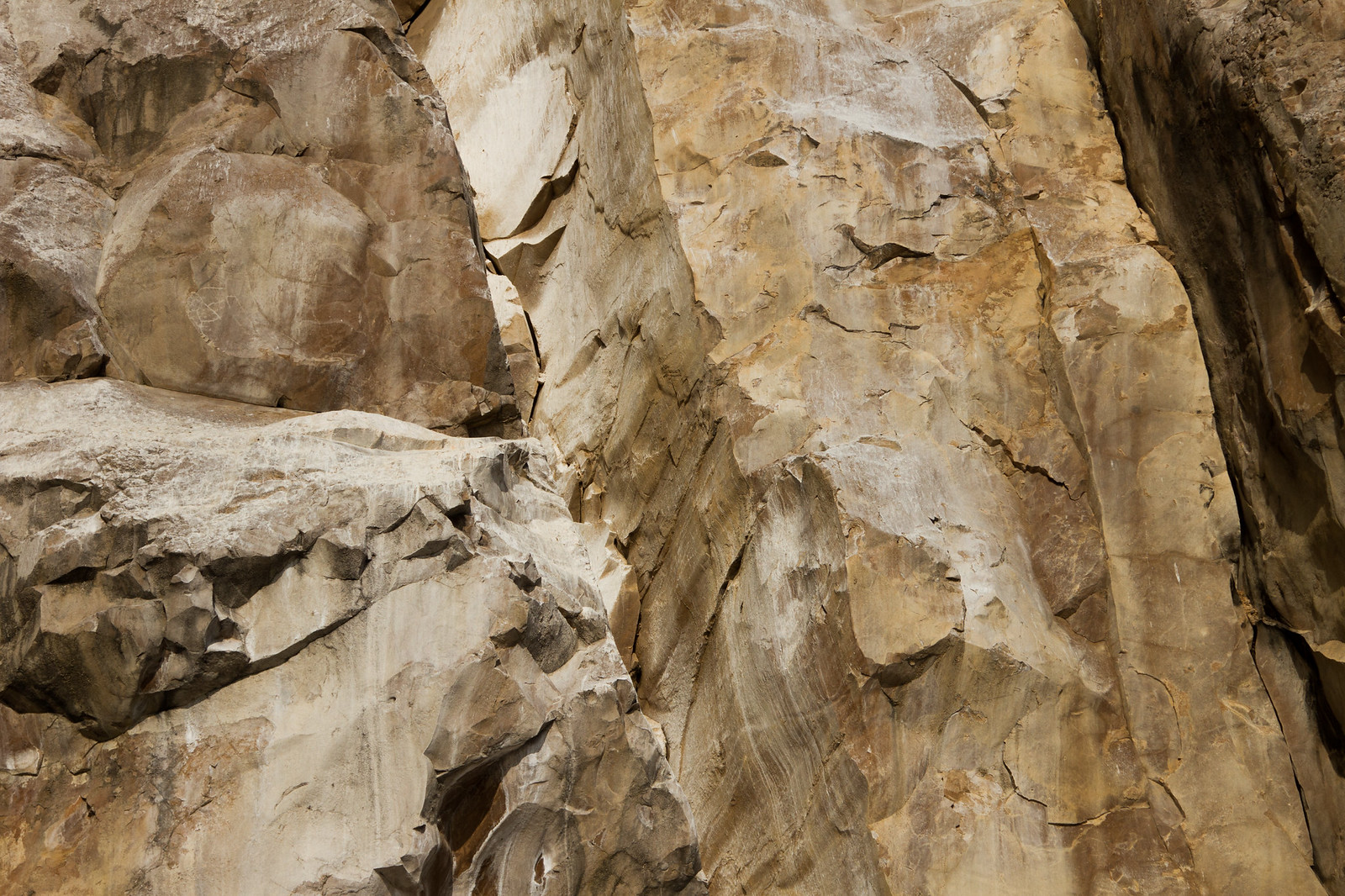 Close-up of a weathered, cracked tan and grey rock face with jagged fractured surfaces