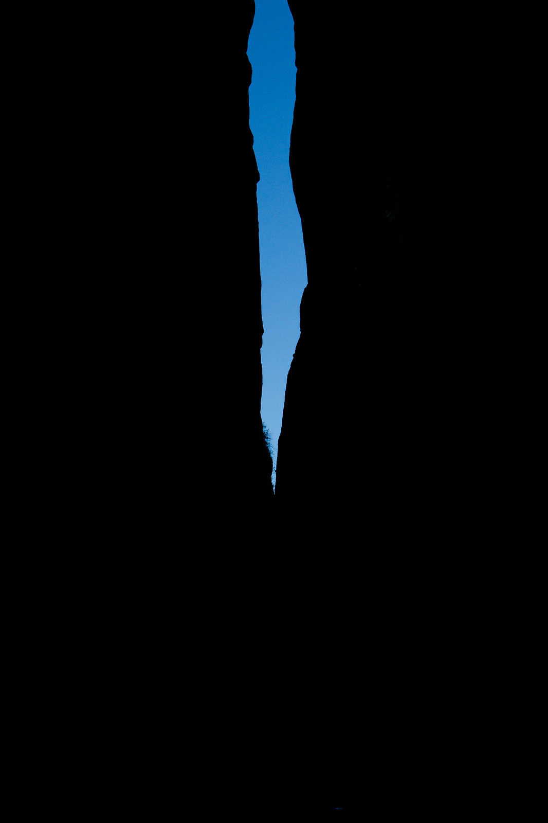 A narrow sliver of blue sky glimpsed between towering silhouetted rock walls of a slot canyon.