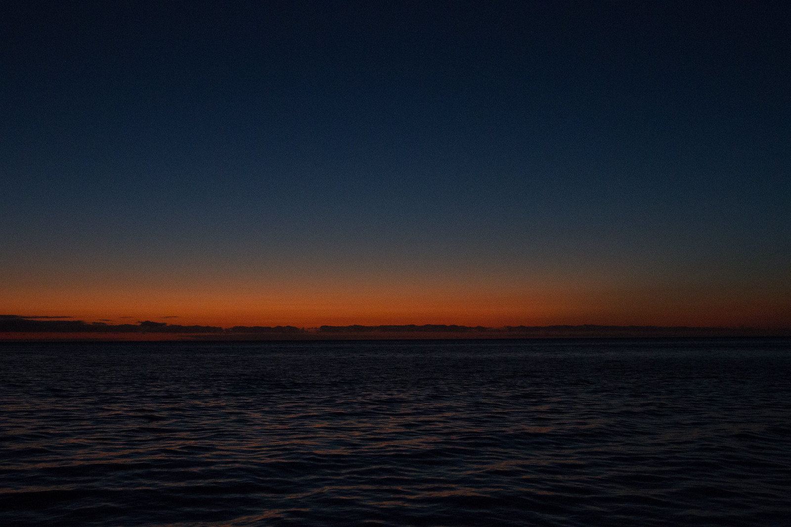 Dusky ocean at twilight with a burnt-orange band of afterglow glowing along the horizon.