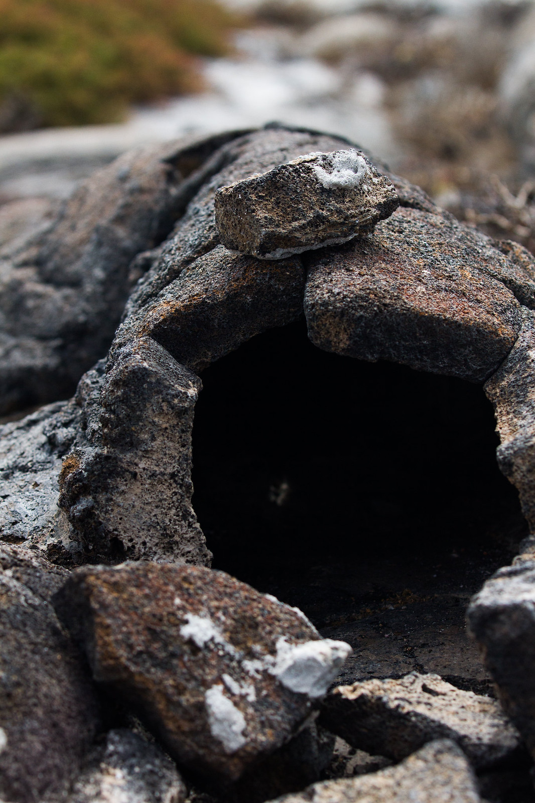 A small arched burrow built from stacked volcanic rocks, its dark opening framed by weathered stones.