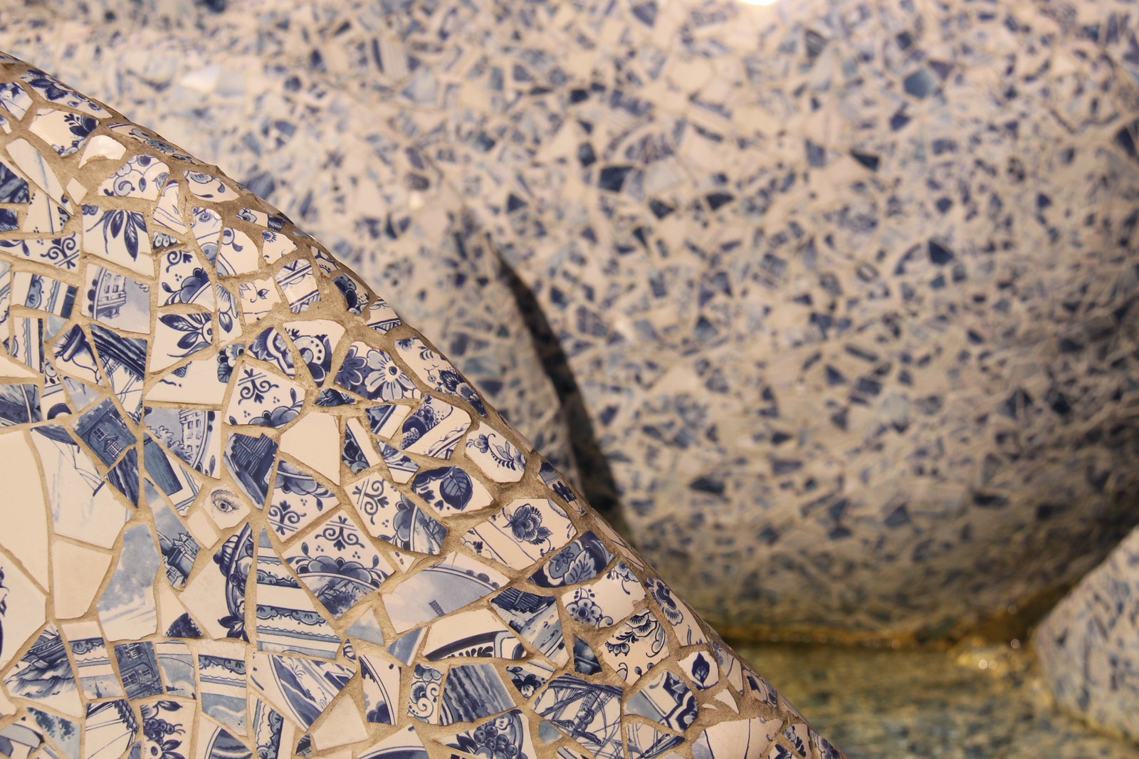Close-up of a fountain sculpture clad in broken blue-and-white Delft porcelain shards forming a mosaic.
