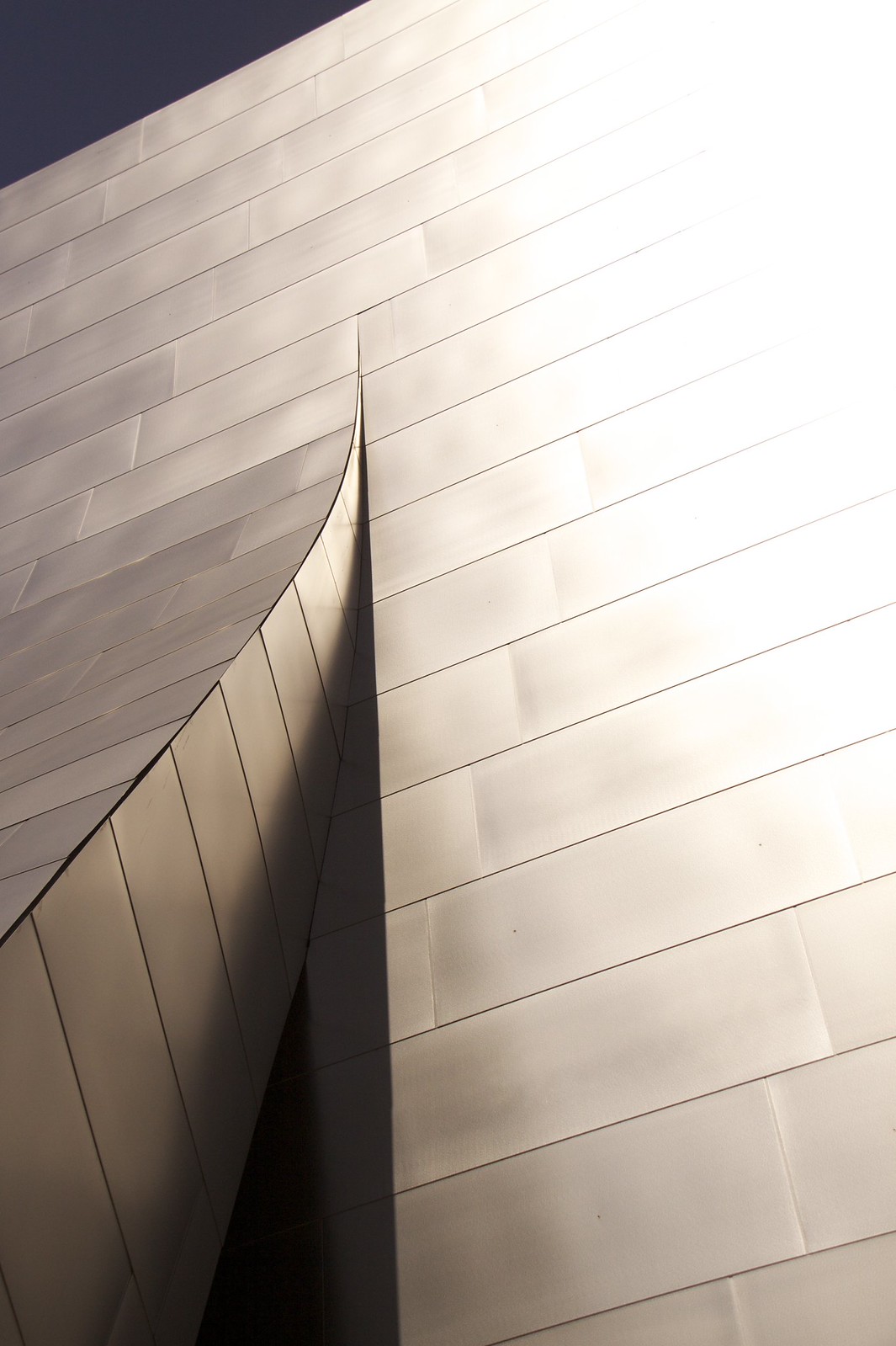 Curving stainless-steel panels of a Frank Gehry facade meeting at a sharp vertical edge against a dark sky.