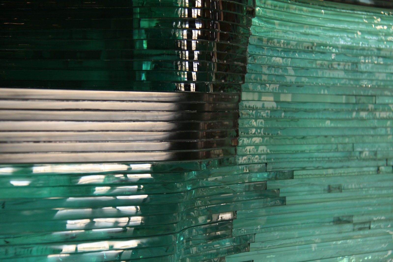 Close-up of stacked layers of green glass sheets, their edges catching light and reflections.