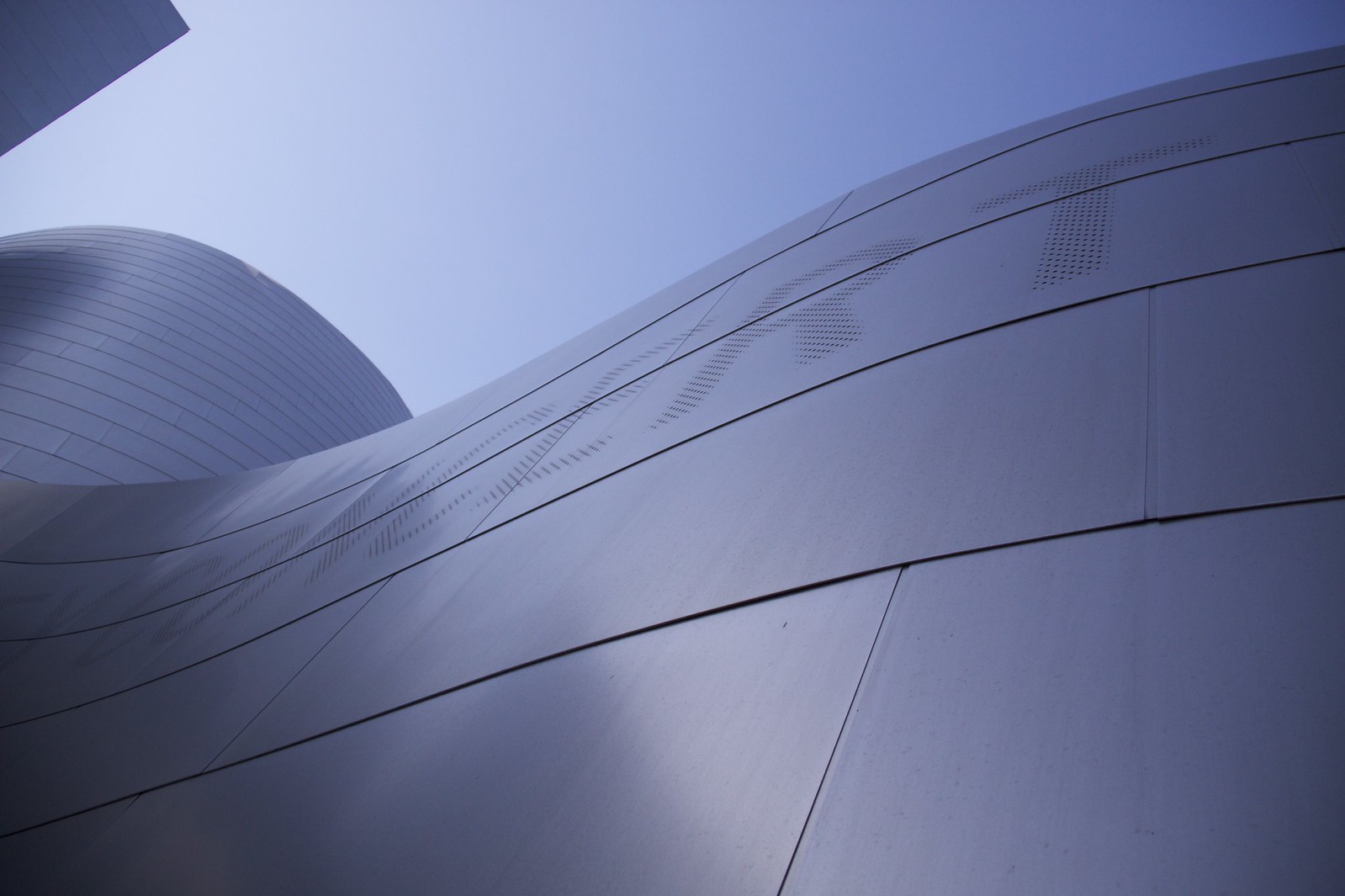 Sweeping curves of a brushed stainless-steel Gehry facade rising against a clear blue sky.
