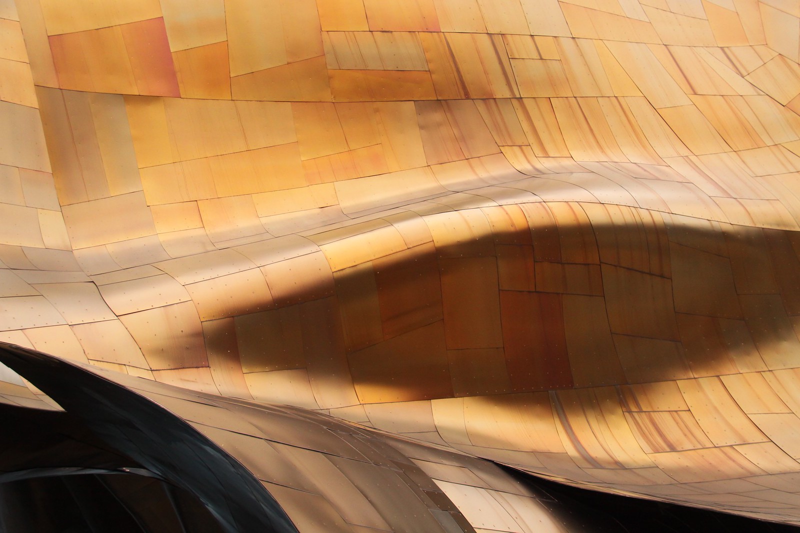 Curved gold and bronze metal panels of Gehry's EMP building forming a rippling abstract skin.