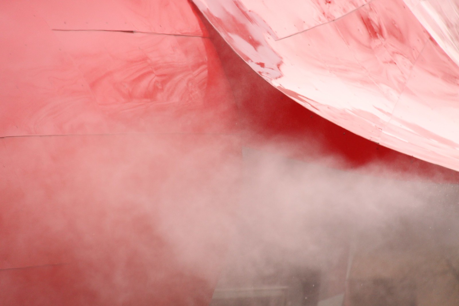 Curving red-painted metal panels of a Gehry structure wreathed in drifting white mist.