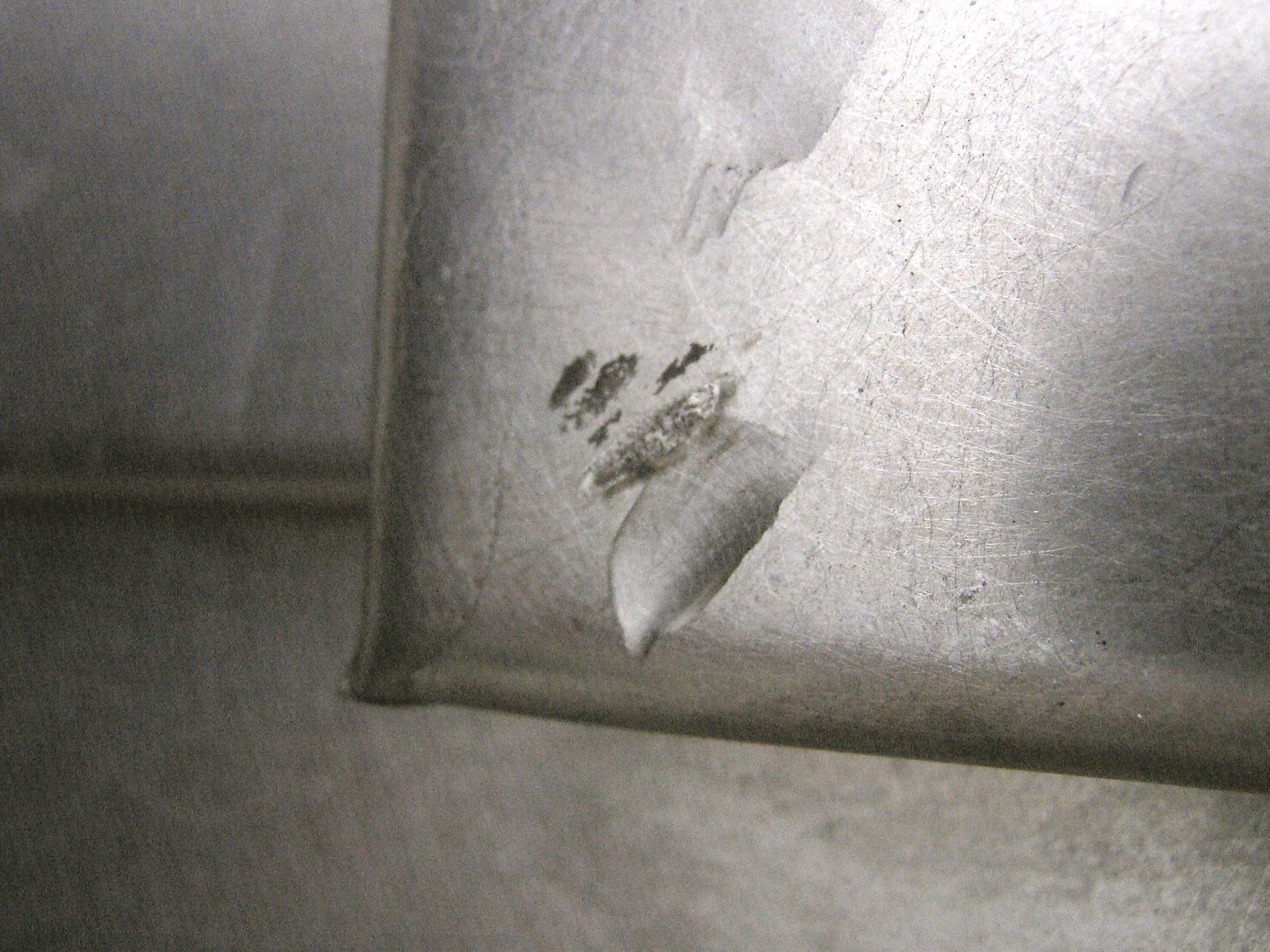 Close-up of a scratched, dented brushed-metal panel with a gouge and small scuff marks.