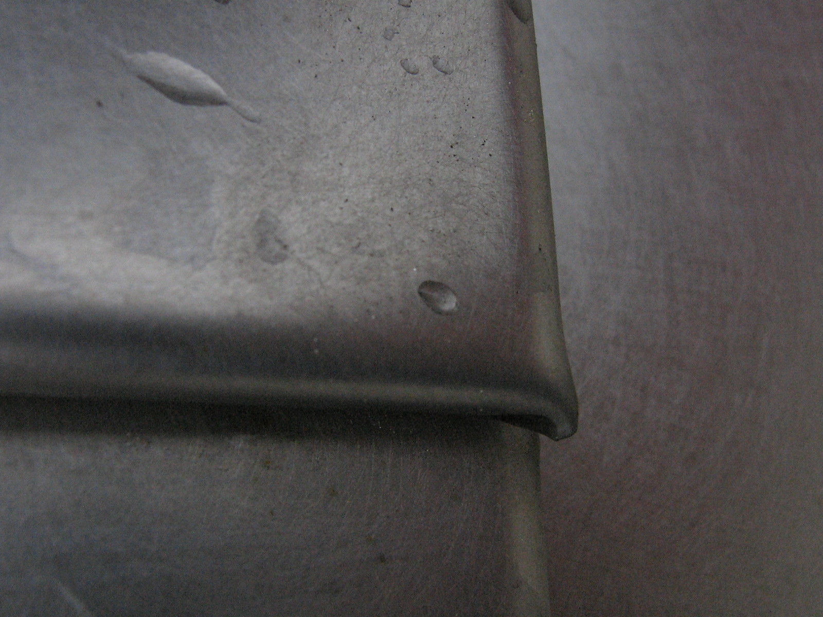Close-up of overlapping grey titanium cladding tiles with rounded edges and scattered water droplets.