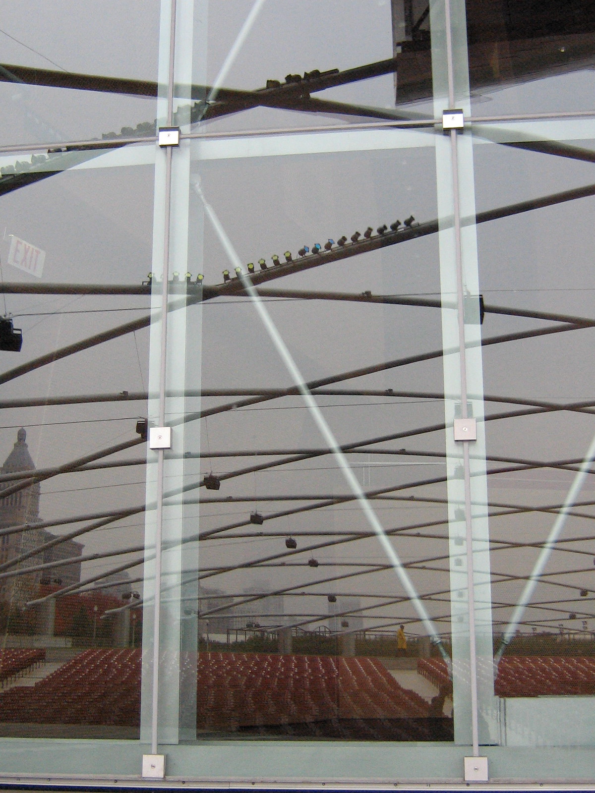 Gehry's crisscrossing steel trellis over Millennium Park's Pritzker Pavilion seating, seen through a glass wall marked "EXIT