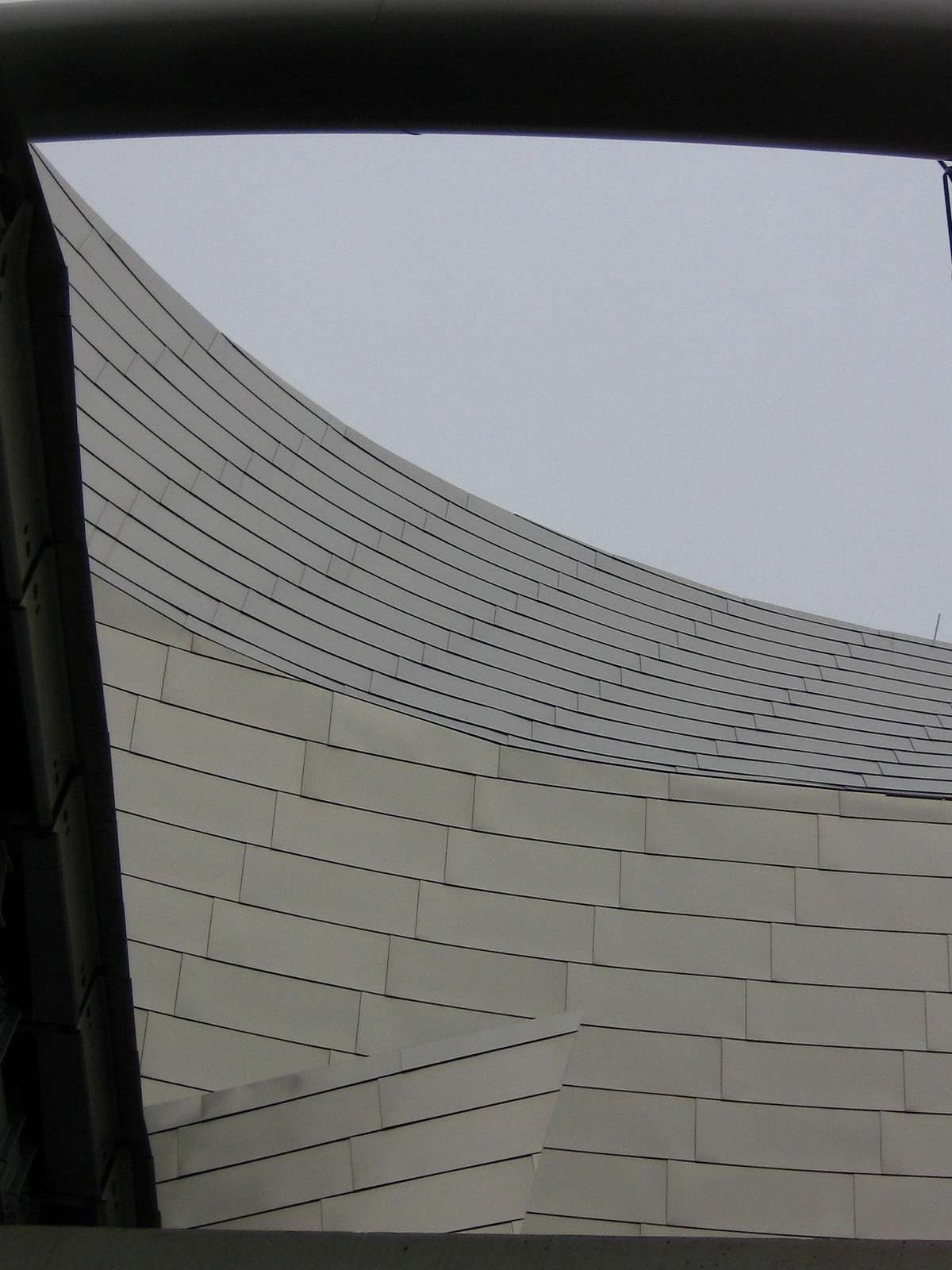 Sweeping curved metal-panel facade of a Frank Gehry building framed against an overcast grey sky.