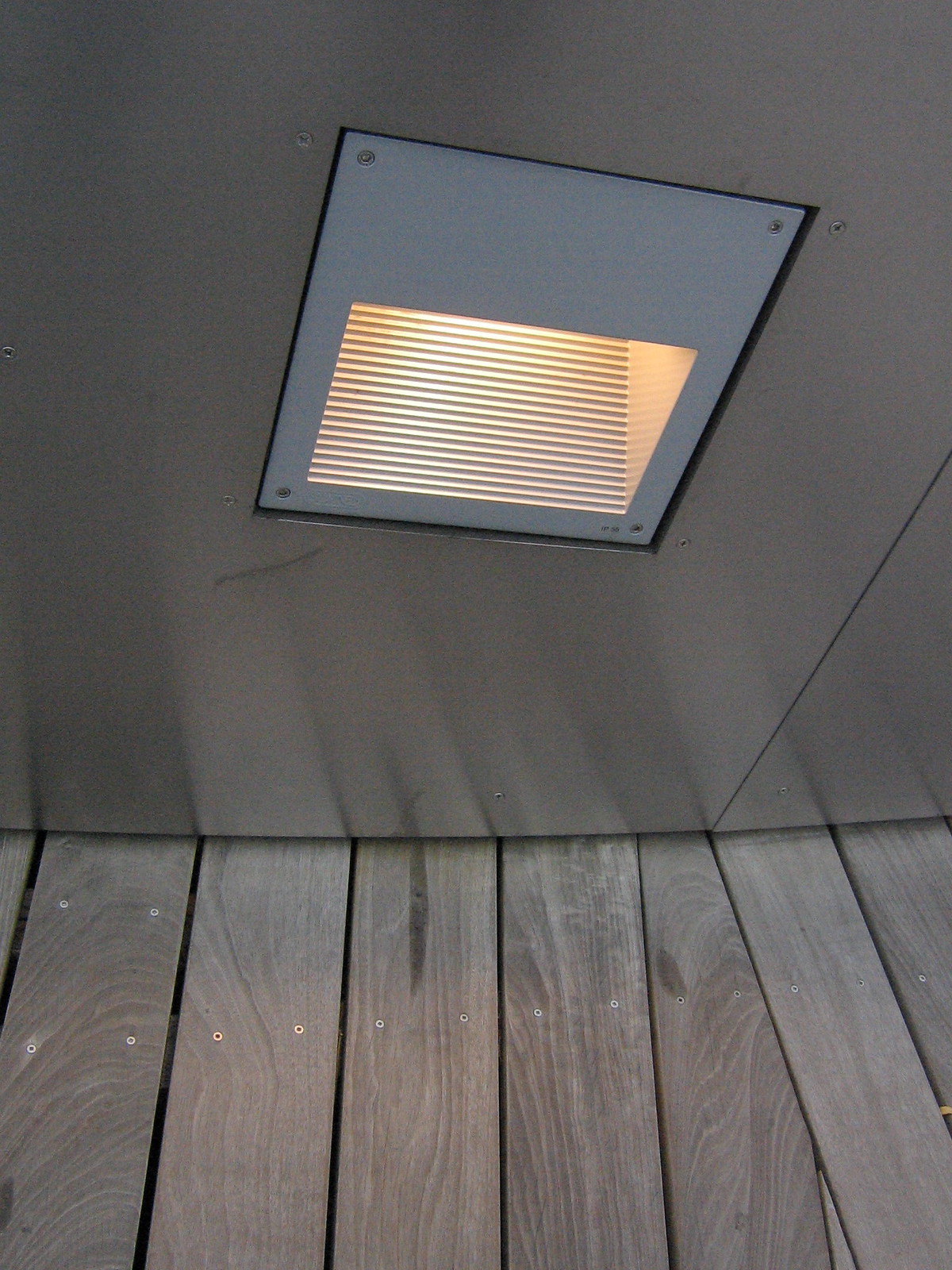 Recessed square louvered ceiling fixture glowing warm above weathered gray wood decking.