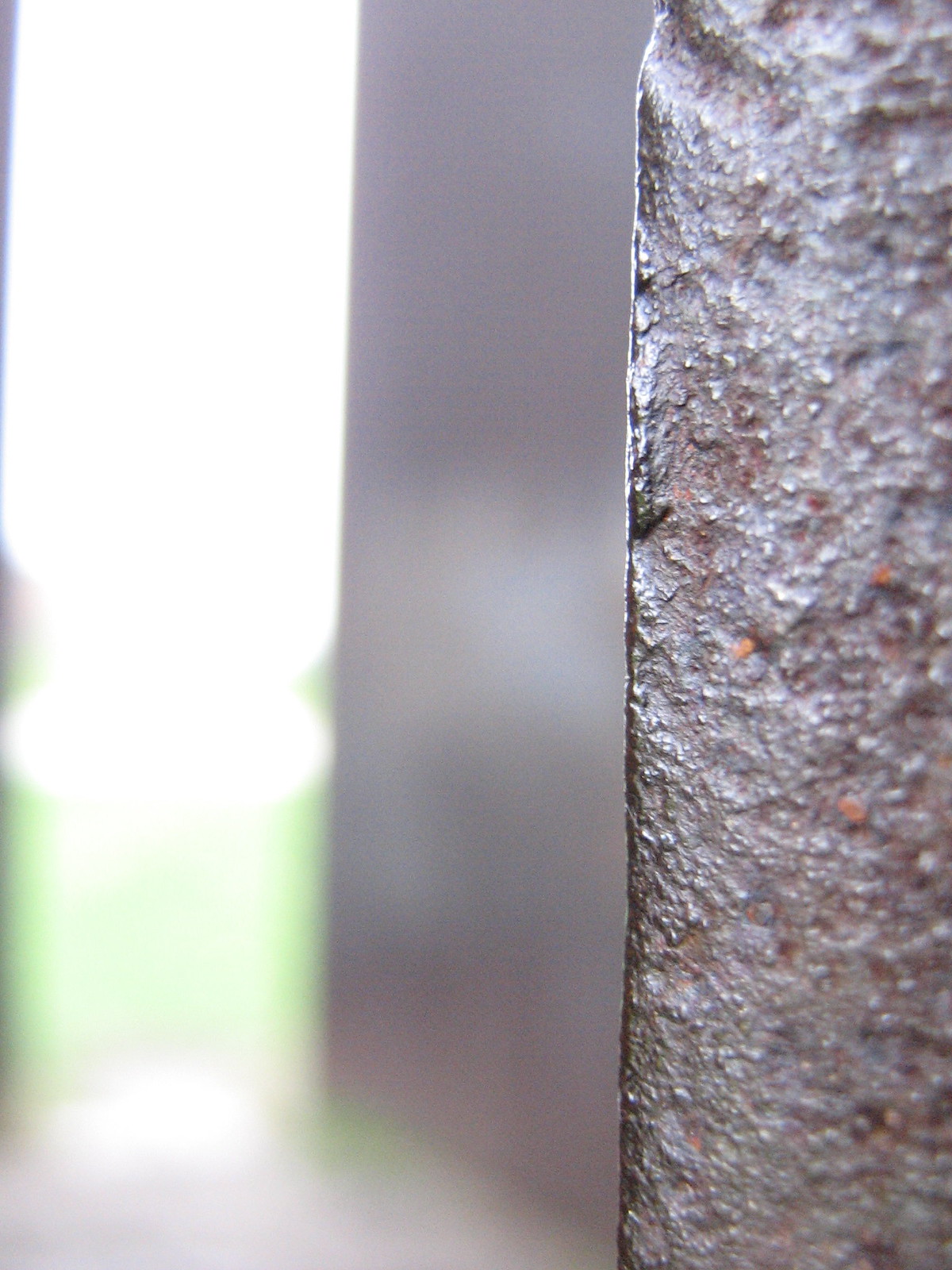 Close-up of a rough, rusted metal edge in sharp focus against a blurred bright background.
