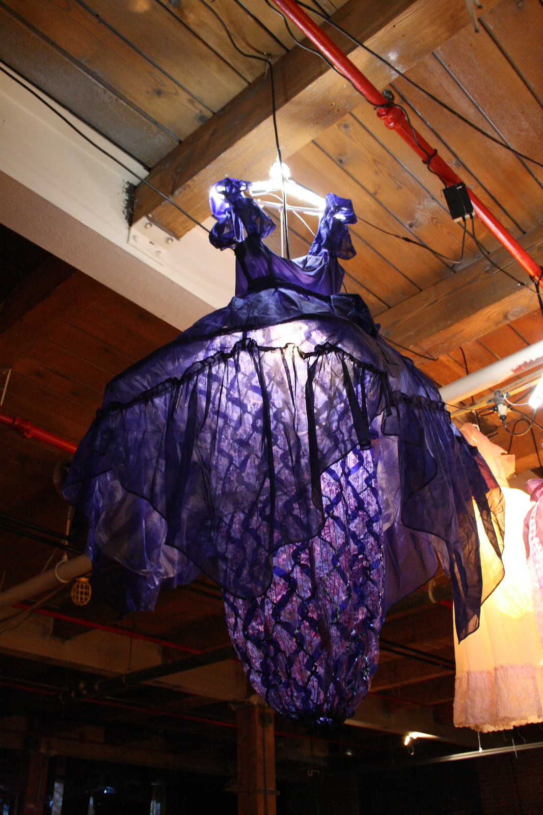 Purple and black organza dress sculpture hanging upside down from a wood-beamed ceiling in a loft gallery.