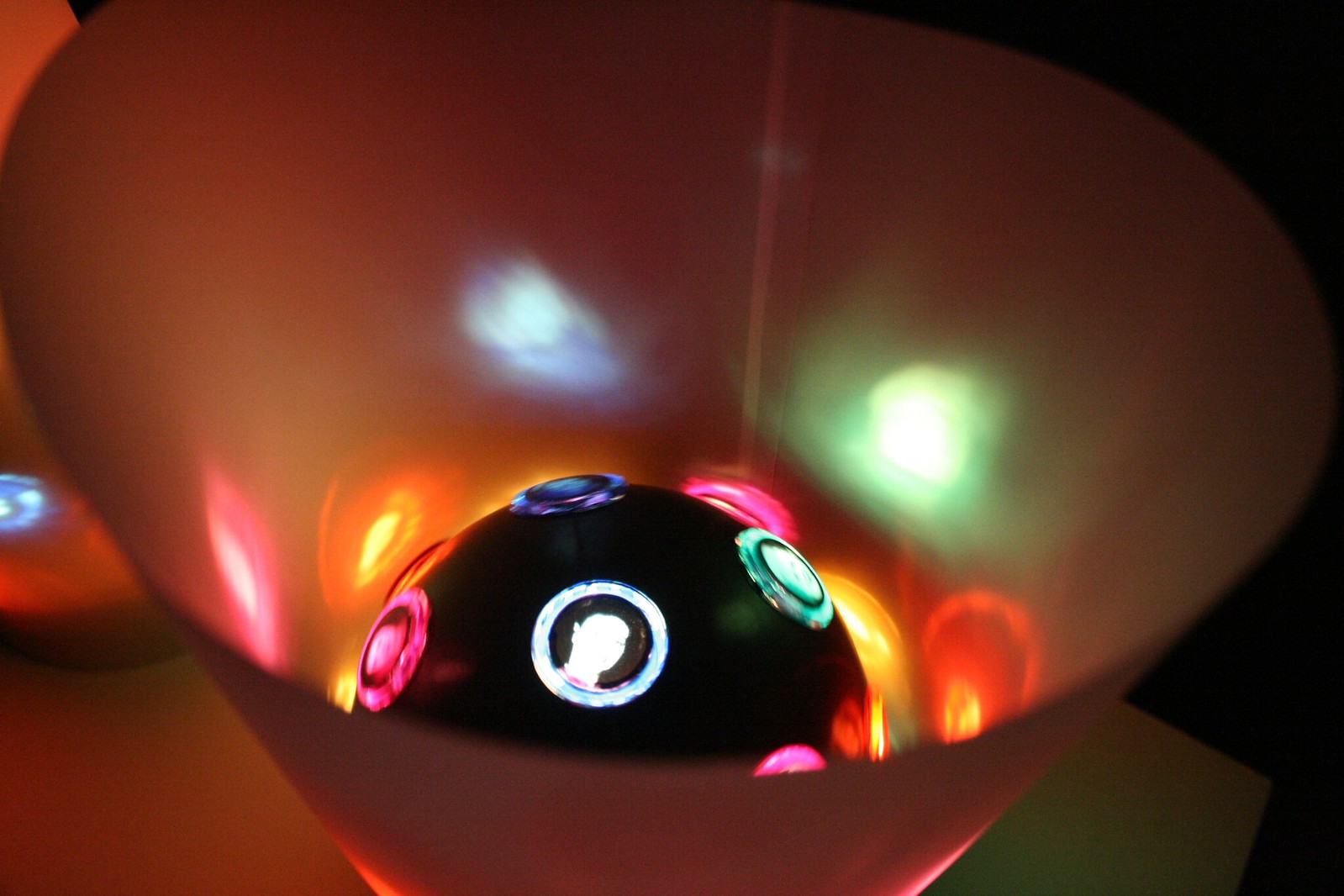 A dome-shaped disco light casting colorful red, green, blue, and pink glows onto a curved white bowl in the dark.