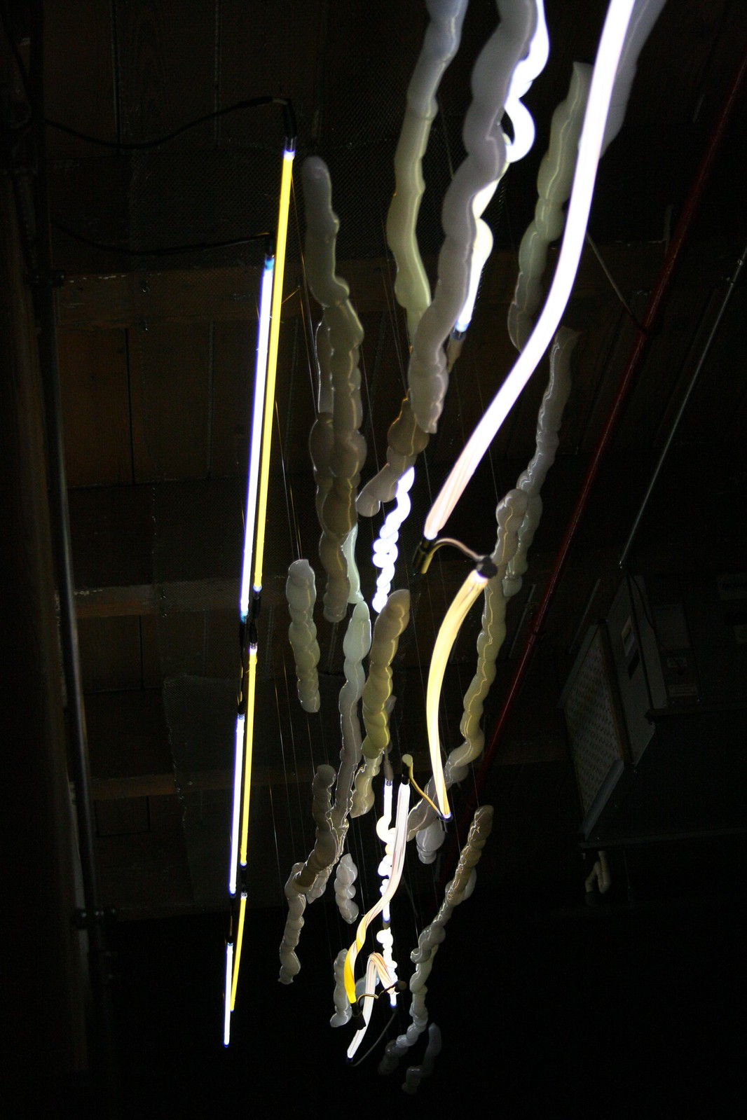 Illuminated neon and frosted-glass sculptures in yellow and white hang from a dark warehouse ceiling.