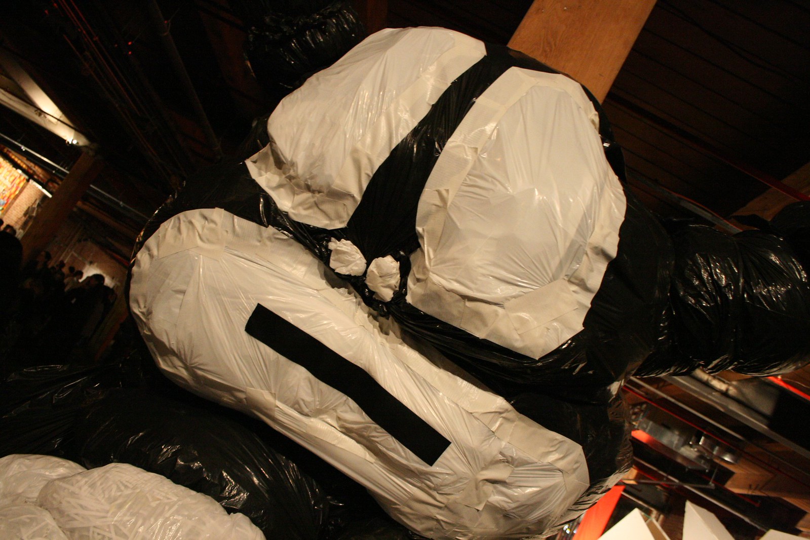 Giant sculpture built from black and white plastic bags and tape in a dimly lit gallery space.