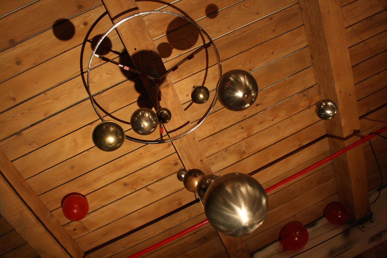 Metal dome pendant lights hang from a wood-plank ceiling with exposed beams and a red pipe.