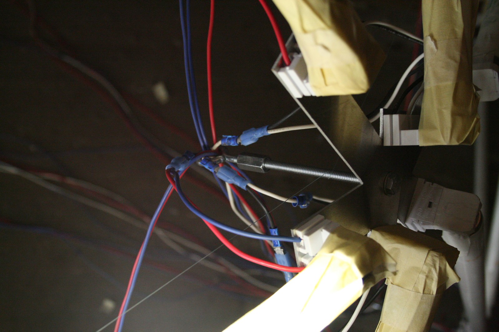 Close-up of tangled red, blue, and white electrical wires with crimp connectors and masking tape on a dark panel.