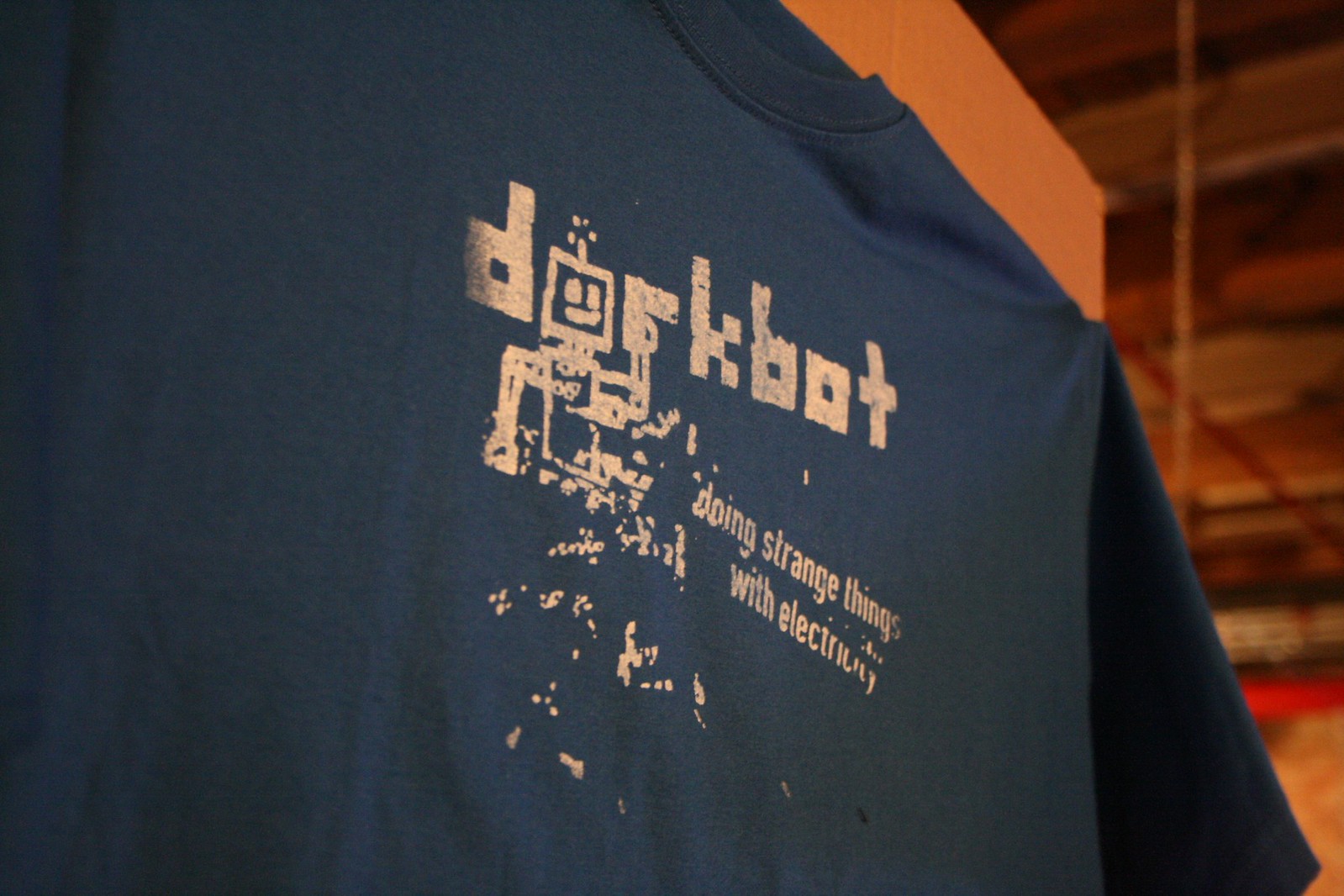 Blue "dorkbot" T-shirt reading "doing strange things with electricity" above a pixelated robot graphic.