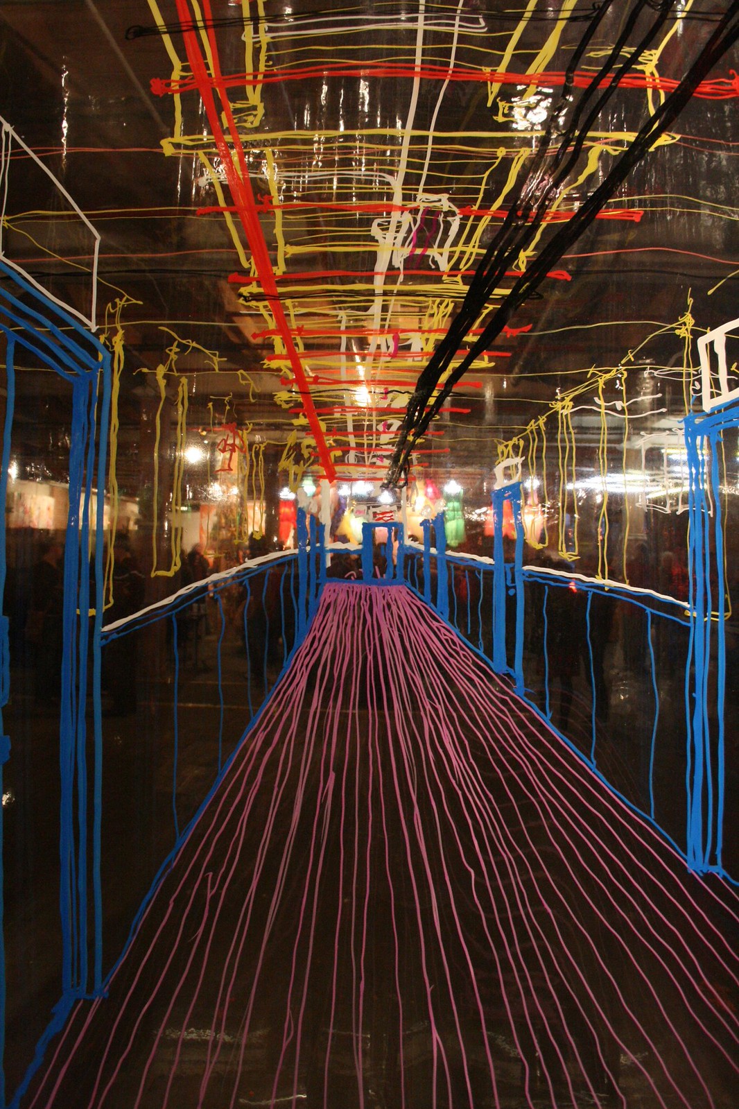 Tape-art corridor drawn in blue, pink, red, and yellow lines over a dark gallery, forming a receding perspective.