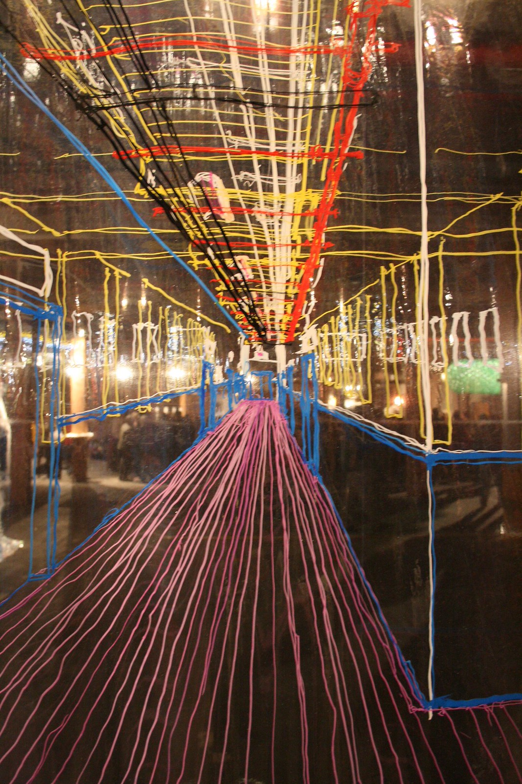 Colorful drawing on glass of a corridor in pink, blue, red and yellow lines over a dark gallery reflection.