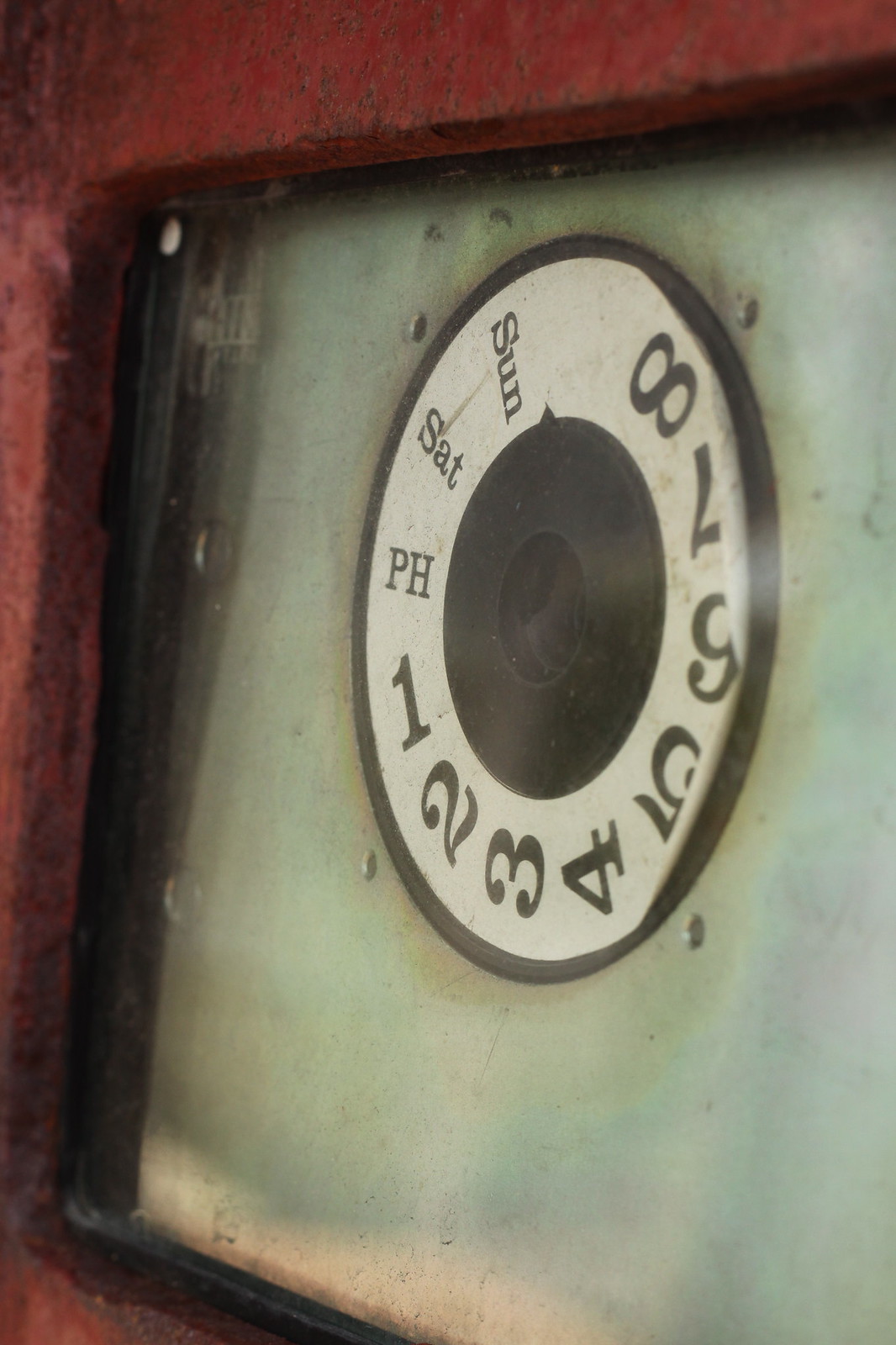 Weathered dial gauge in a red frame with a numbered ring marked Sun, Sat, and PH day labels.