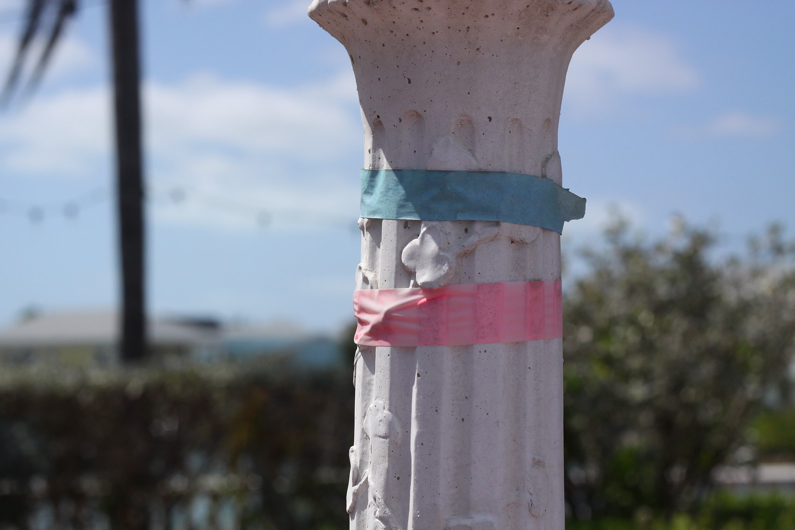 Weathered white pillar wrapped with strips of blue and pink tape against a bright sky.