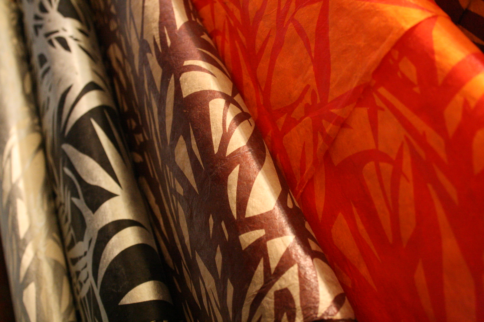 Rolls of Japanese washi paper printed with bamboo-leaf silhouettes in white, black, brown, and glowing orange-red.