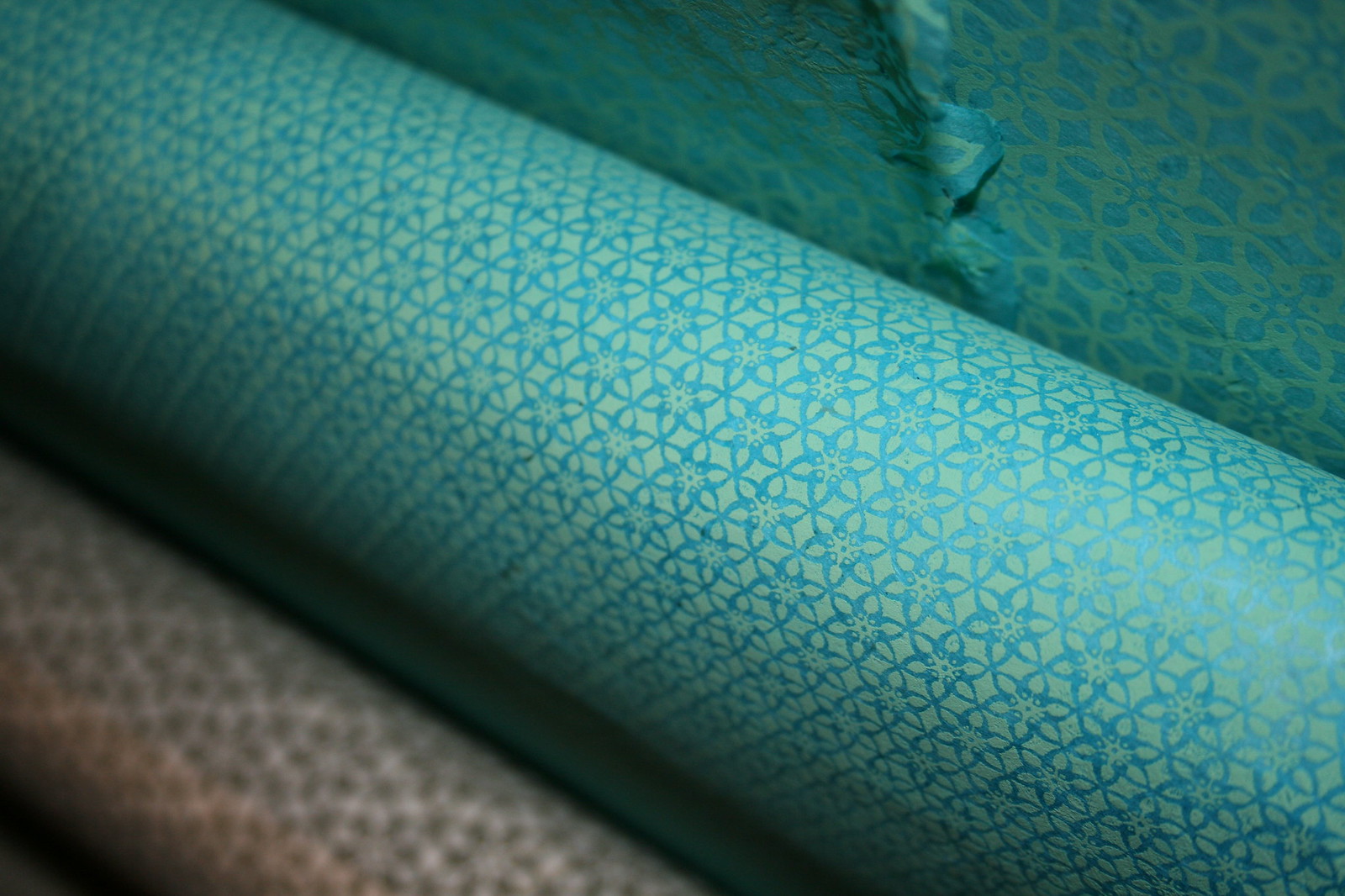 Rolls of teal Japanese paper printed with intricate blue geometric floral patterns, softly lit.