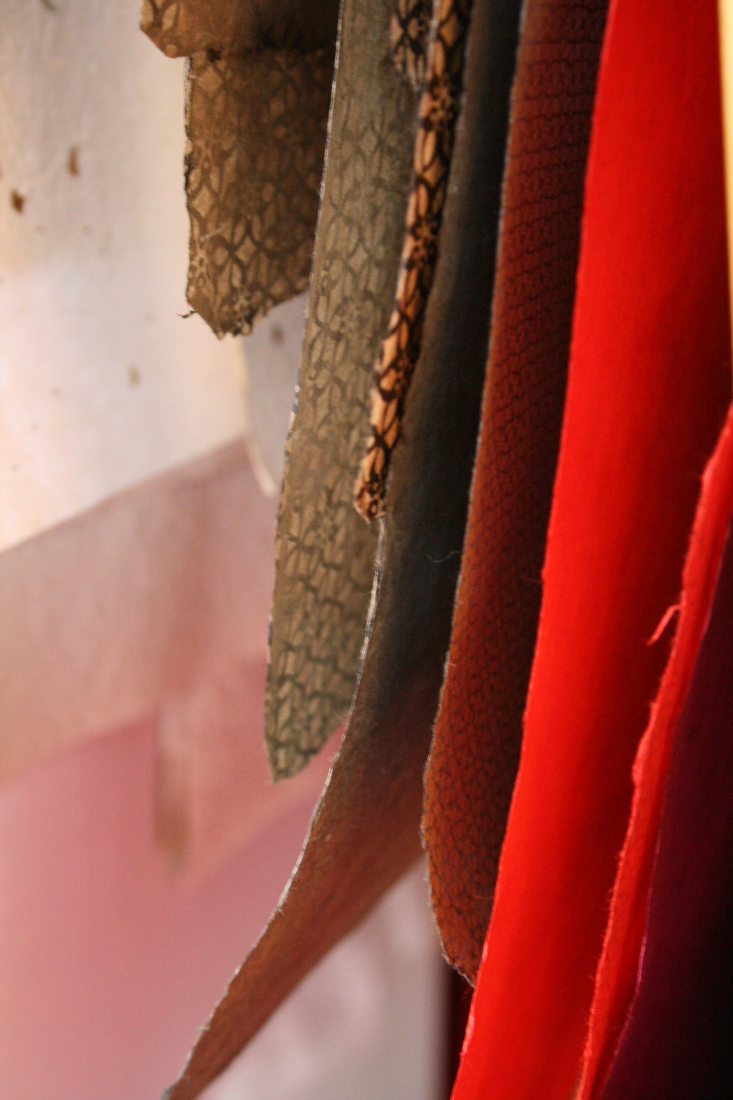 Sheets of textured, lace-patterned handmade Japanese paper in olive, rust, and bright red hang layered together.