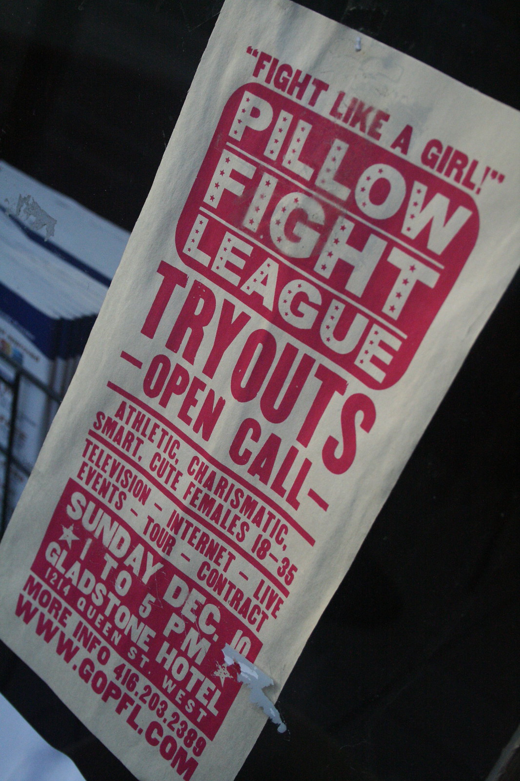 Red-and-white "Fight Like a Girl!" Pillow Fight League tryouts poster taped to a dark surface.