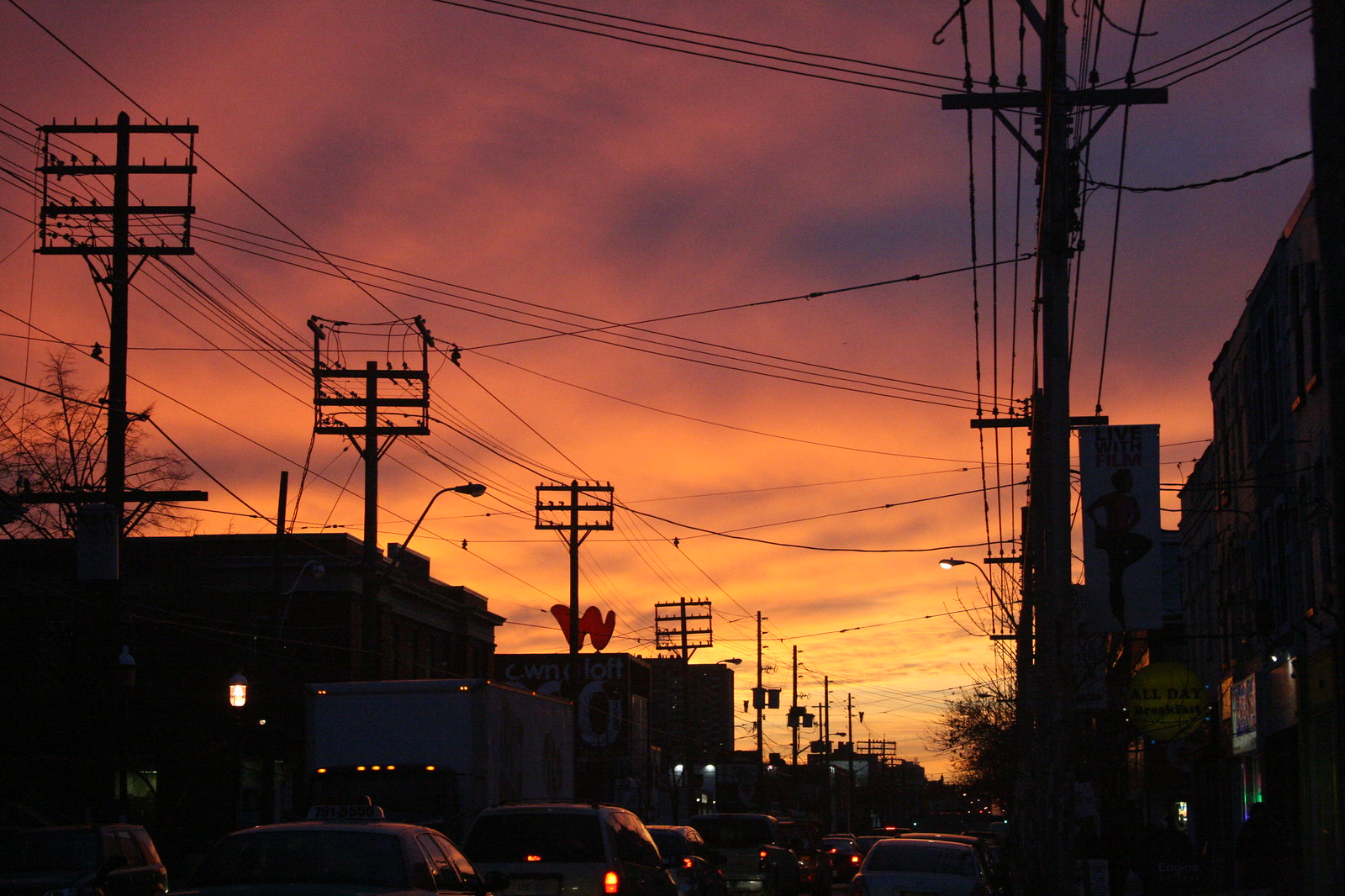 Fiery orange and purple sunset over a city street silhouetting utility poles, wires, and traffic.