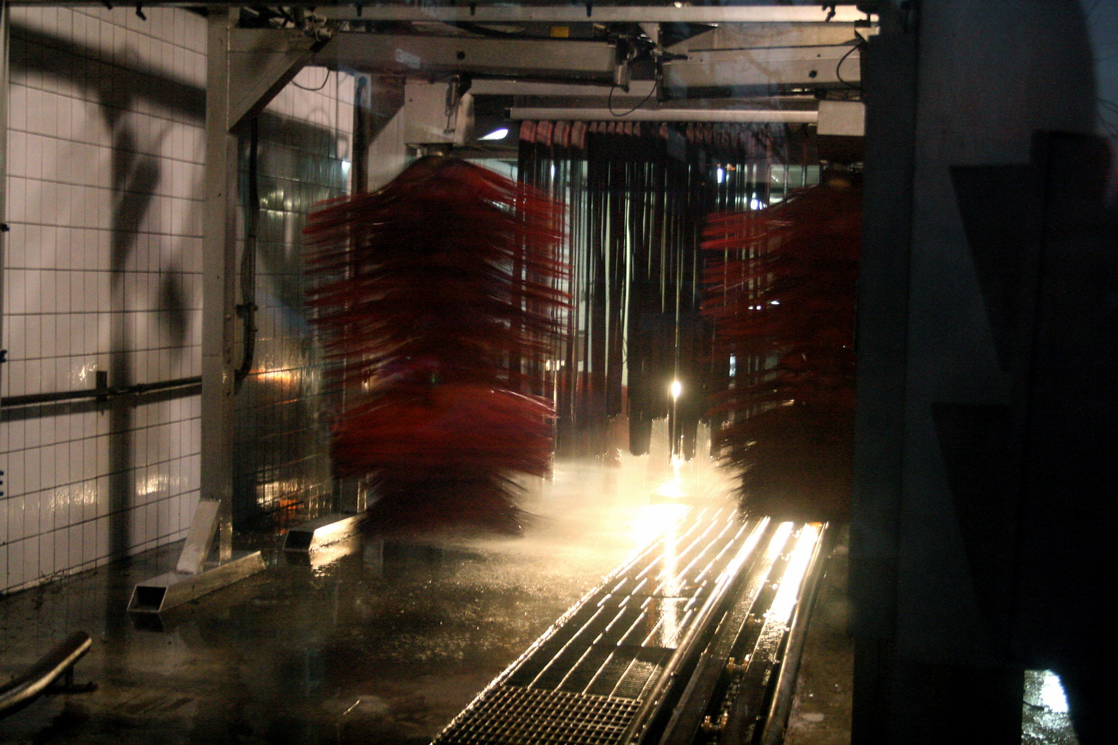Red spinning brushes and cloth strips inside a dimly lit automatic car wash tunnel.