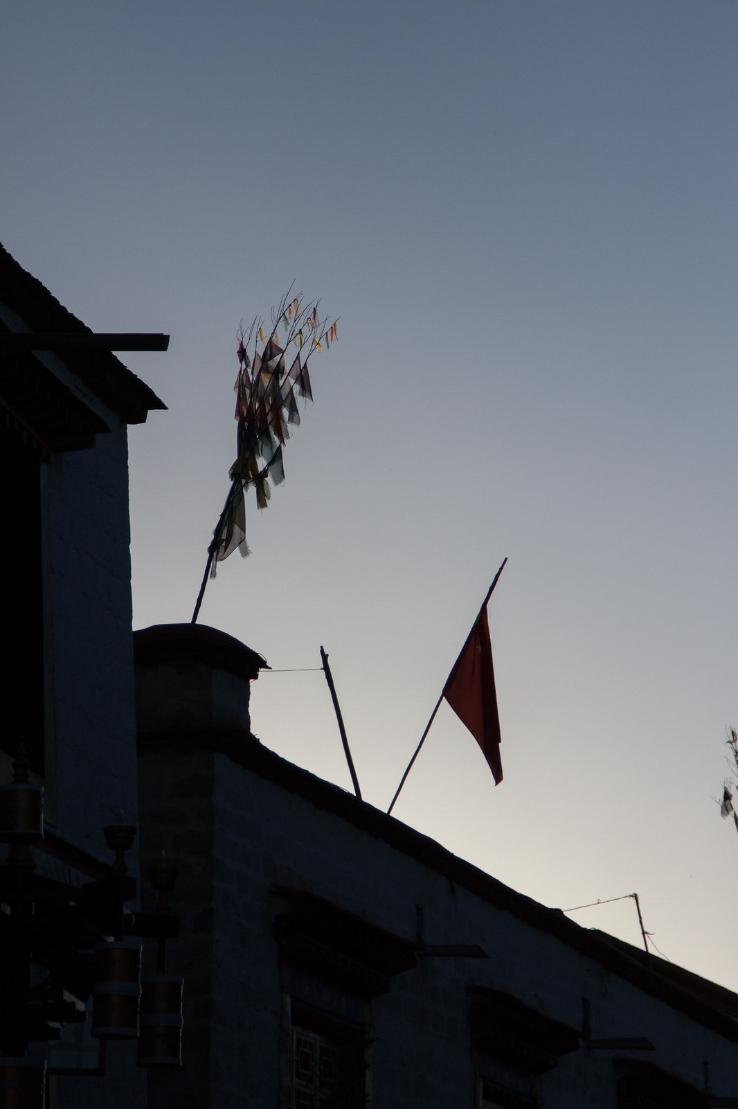 Tibetan prayer flags and a Chinese flag on a rooftop silhouetted against dusk sky