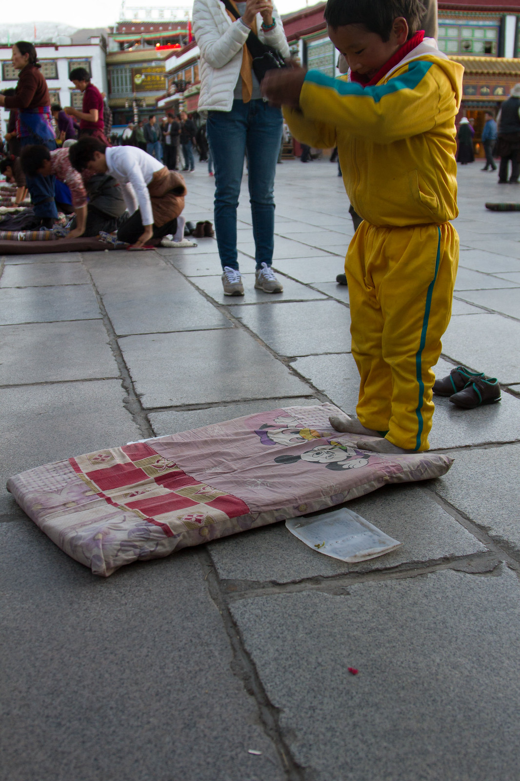 A boy in a yellow tracksuit prostrates on a prayer mat outside Jokhang Temple in Lhasa.