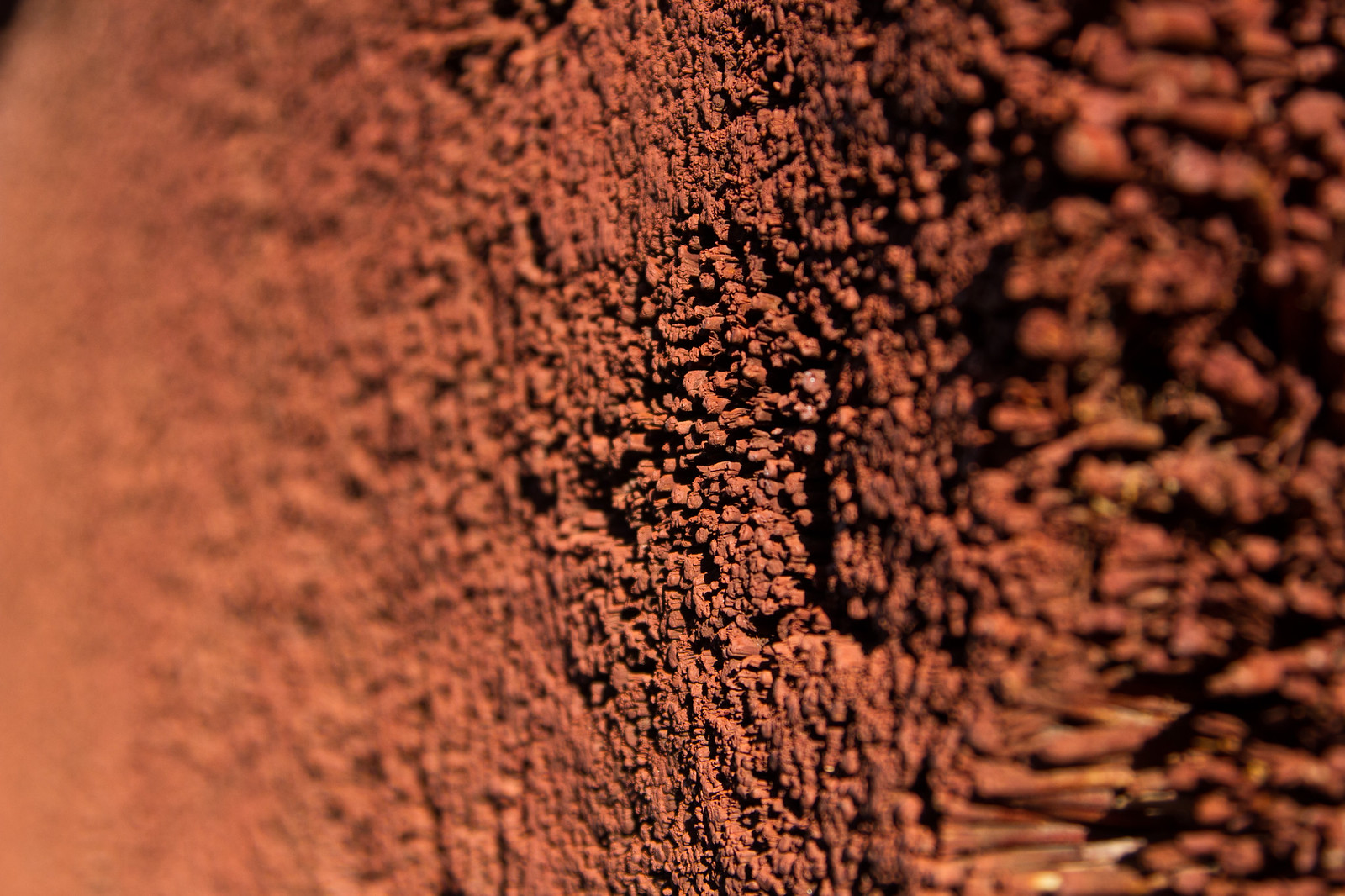 Close-up of textured red clay wall with a ridged, crumbling surface catching warm light