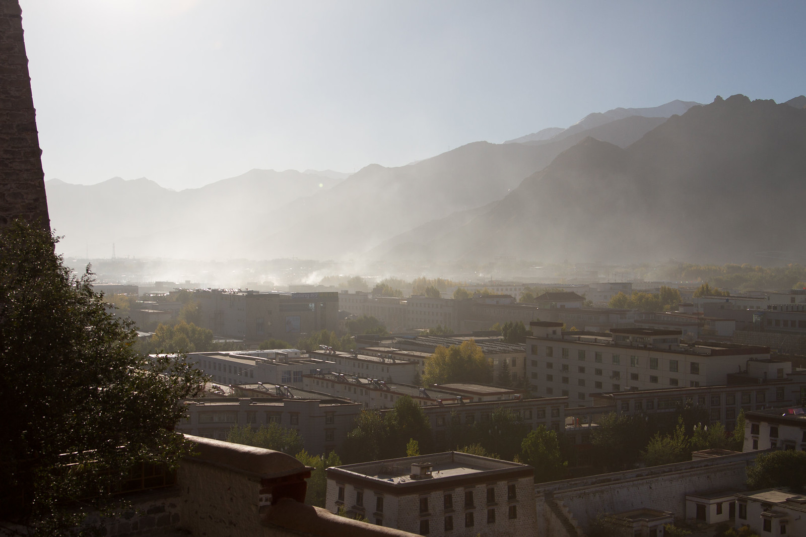 Hazy morning light over Lhasa's rooftops and valley, with mountains rising behind the city.