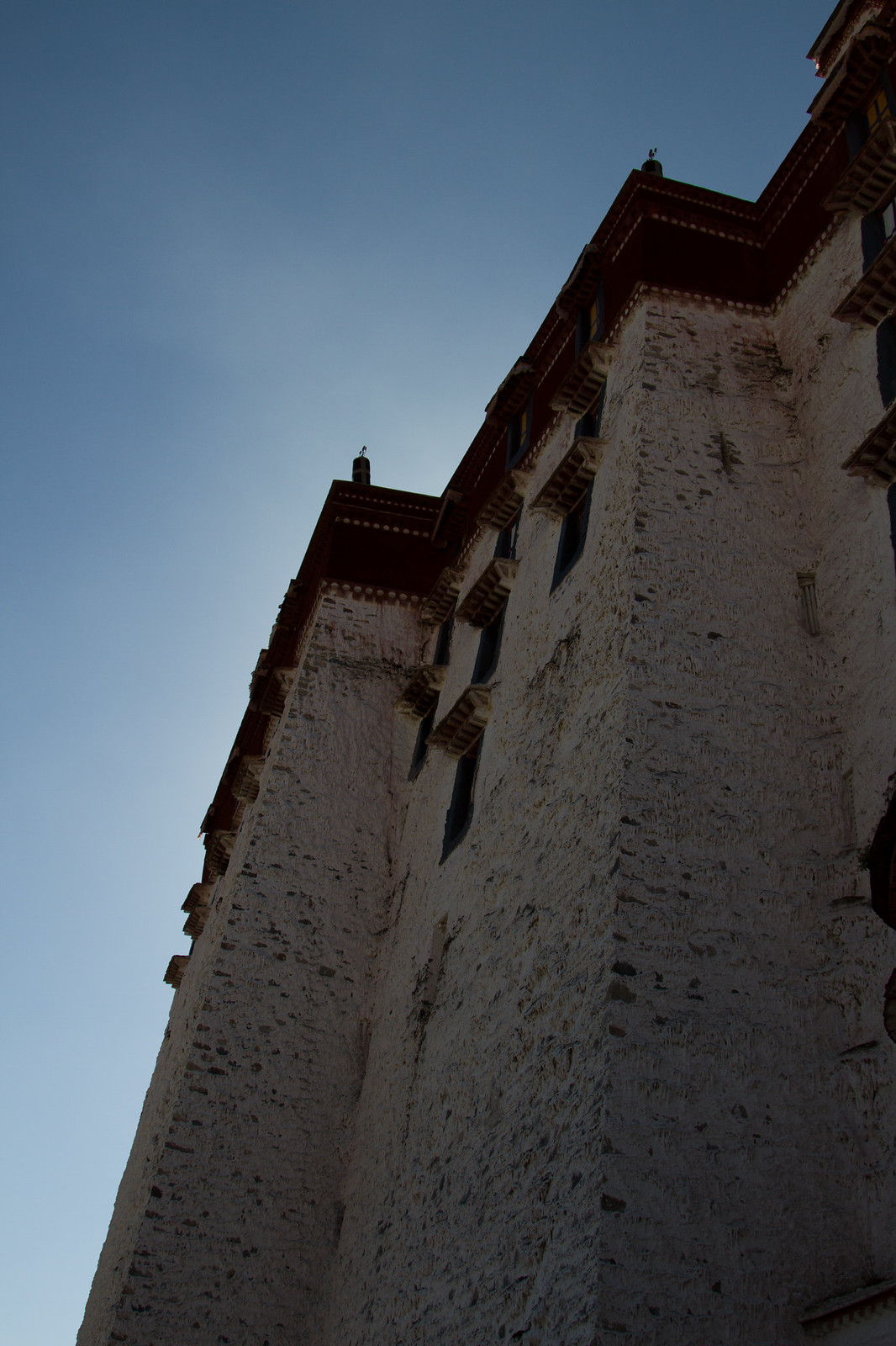 Towering whitewashed wall of the Potala Palace with dark windows and red trim against a clear blue sky.