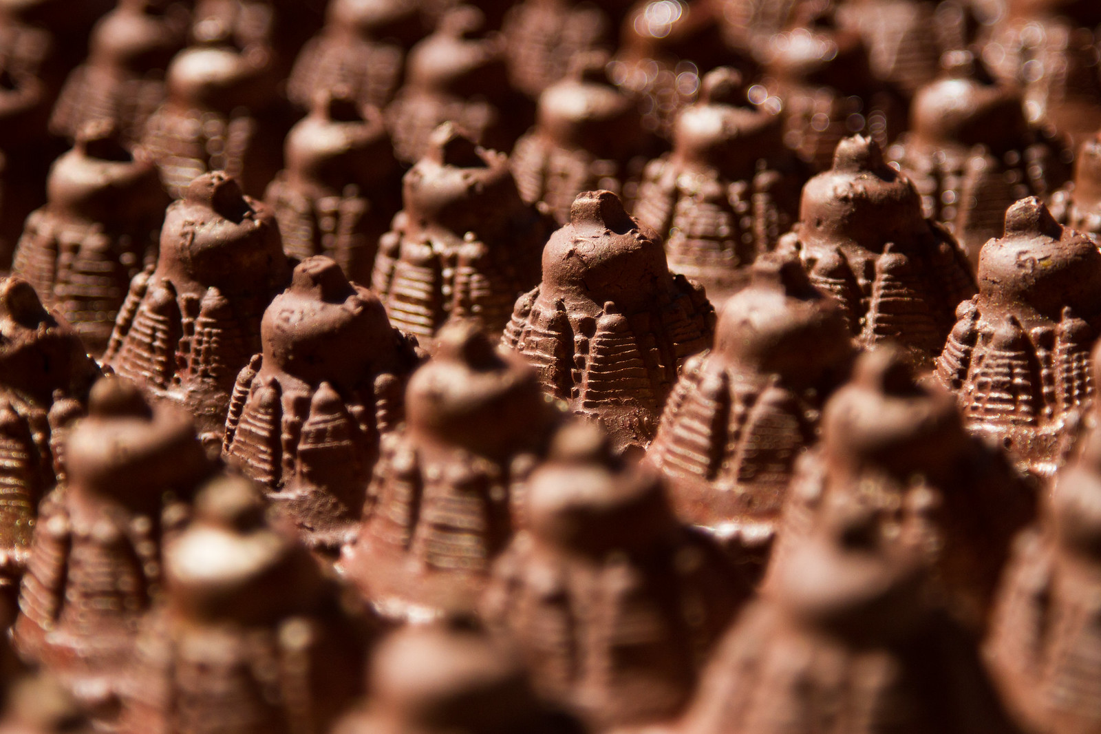 Rows of small hand-molded clay tsatsa votive offerings arranged closely together in warm sunlight.