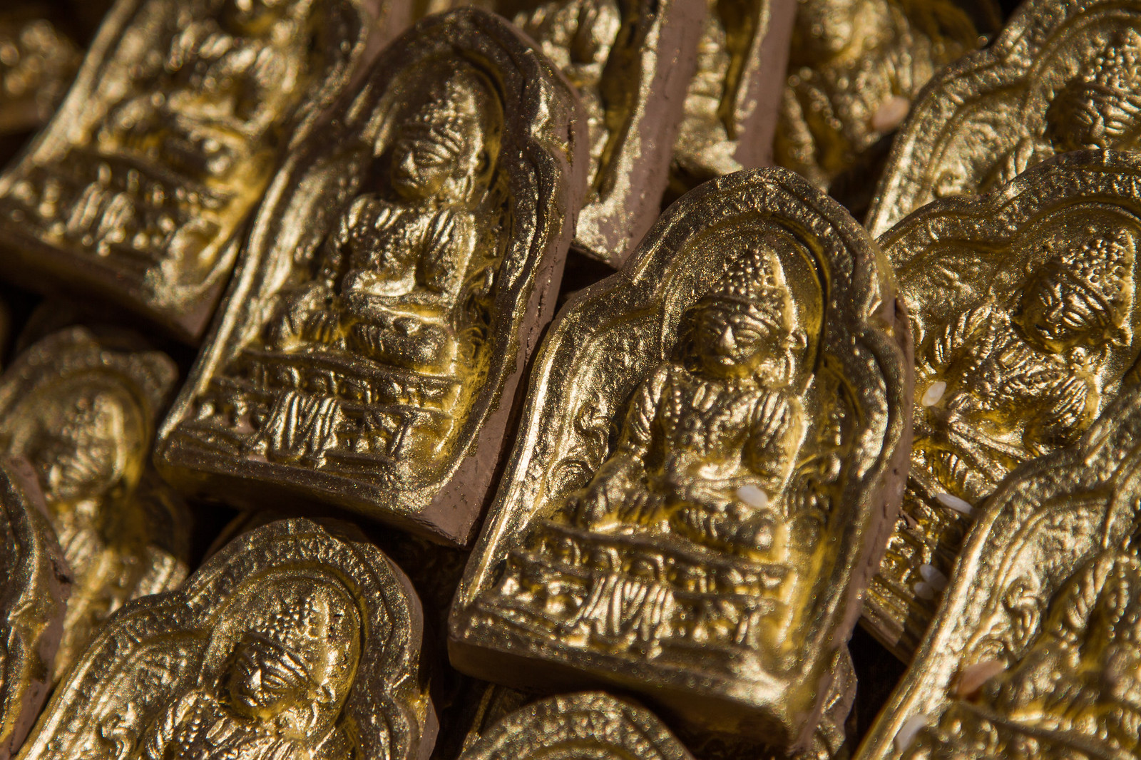 Close-up of a pile of small gold-painted clay tablets each embossed with a seated Buddha figure.