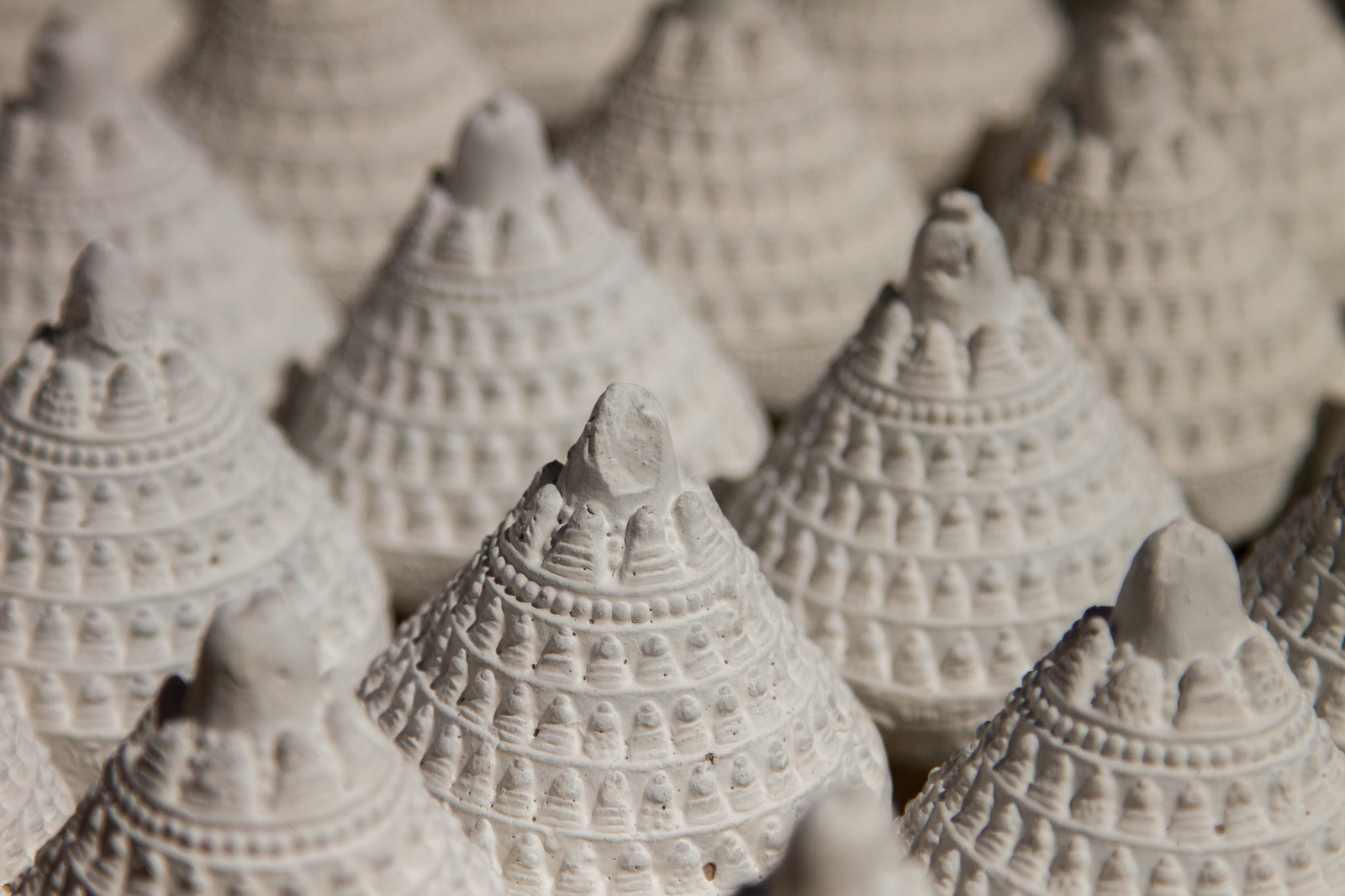 Rows of white clay tsatsa, small conical Tibetan votive offerings pressed with Buddha figures and stupa patterns.