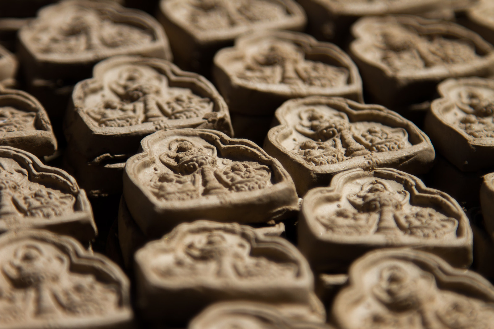 Rows of hand-molded clay tsa-tsa votive tablets embossed with Buddhist stupa and deity reliefs, drying in sunlight.