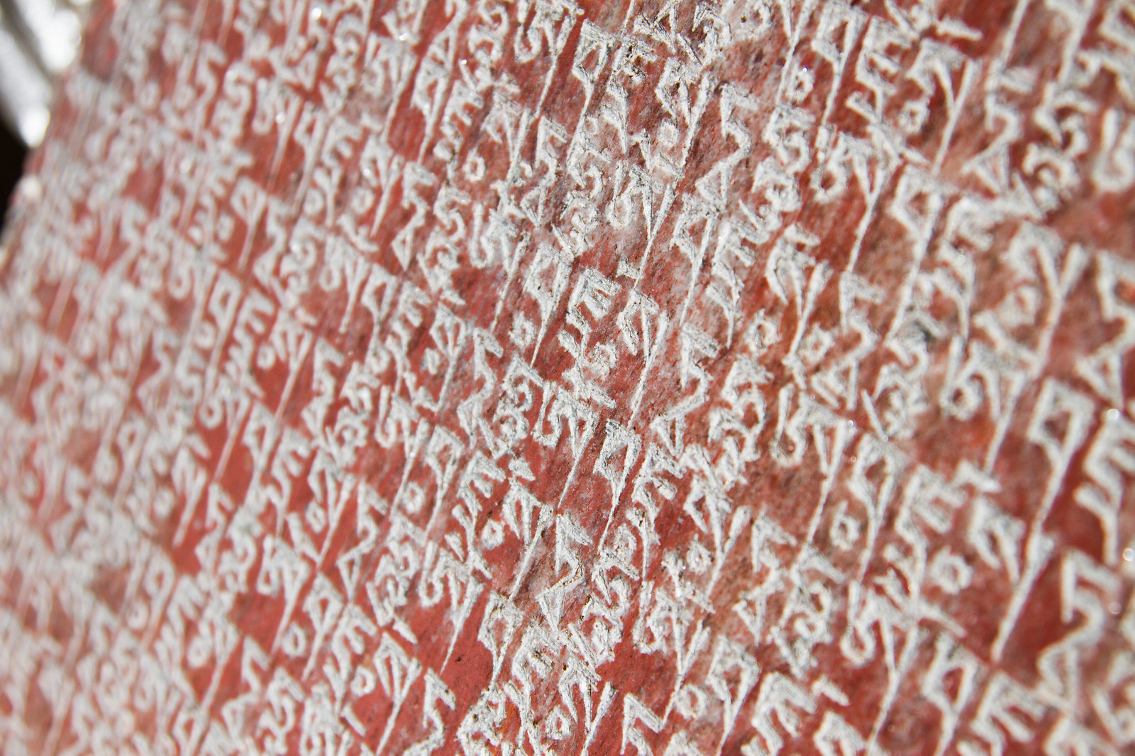 Close-up of Tibetan mantra script carved into a red-painted stone with white lettering.