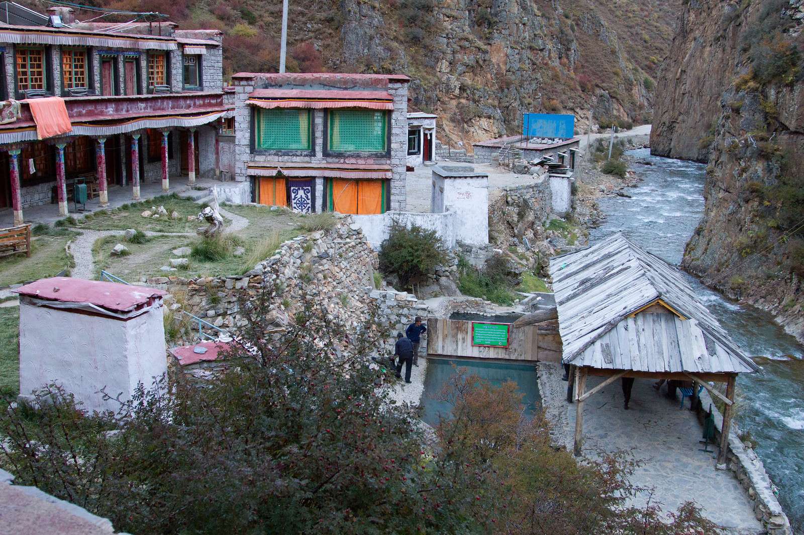 Tibetan hot spring village with colorful stone buildings beside a rushing river in a rocky canyon.