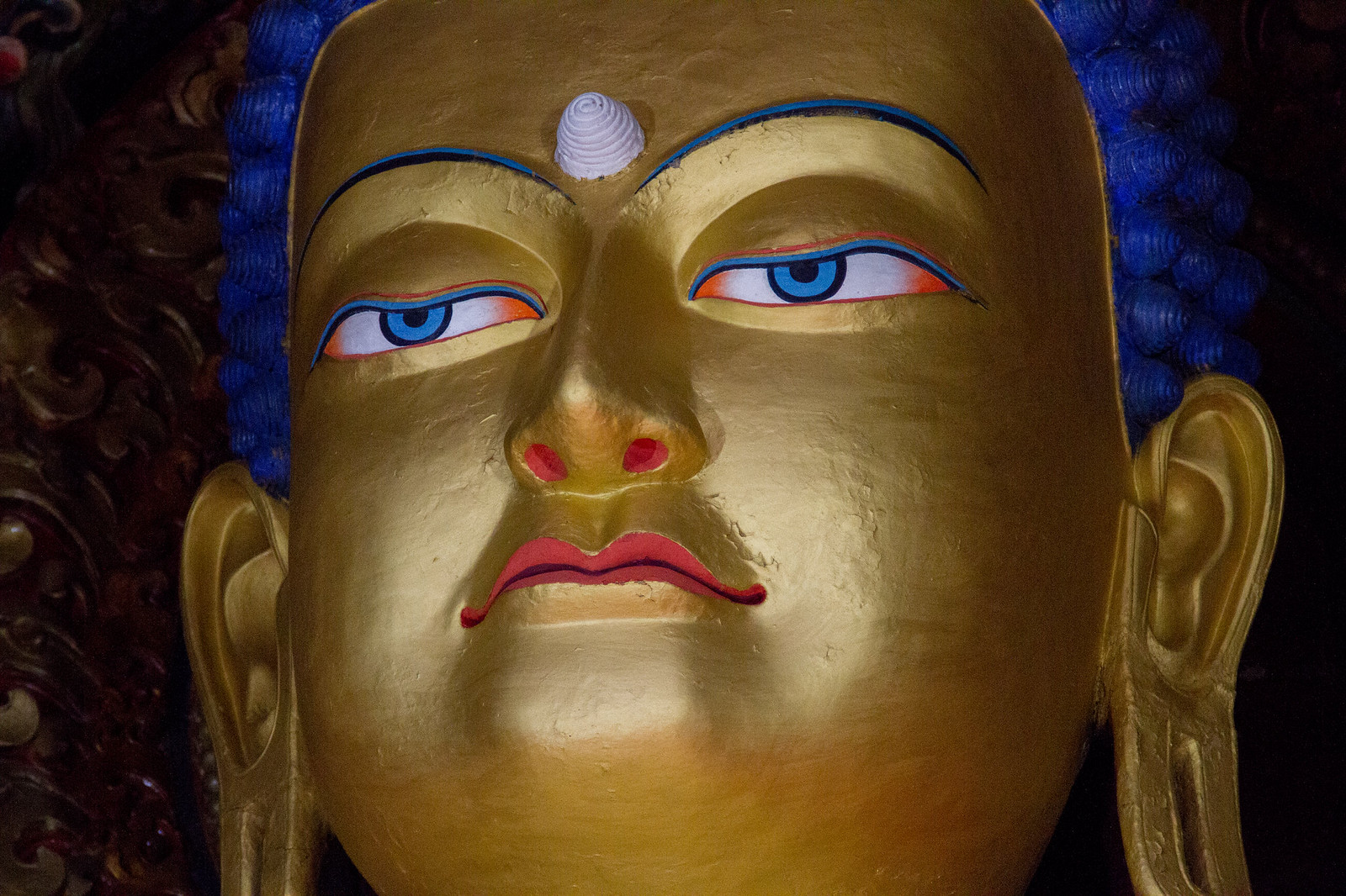 Close-up of a gilded Buddha statue's face with blue hair, painted eyes, and red lips.