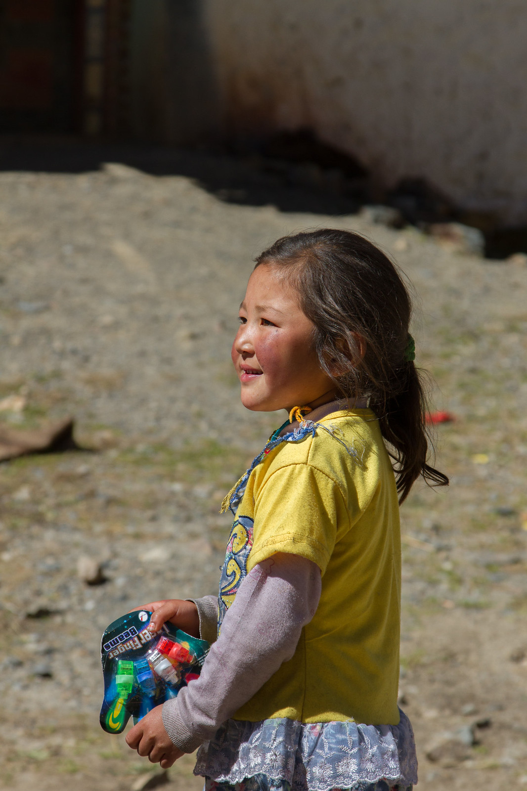 Smiling young girl in a yellow shirt holds a package of "Finger Beams" LED lights on a rocky village path.