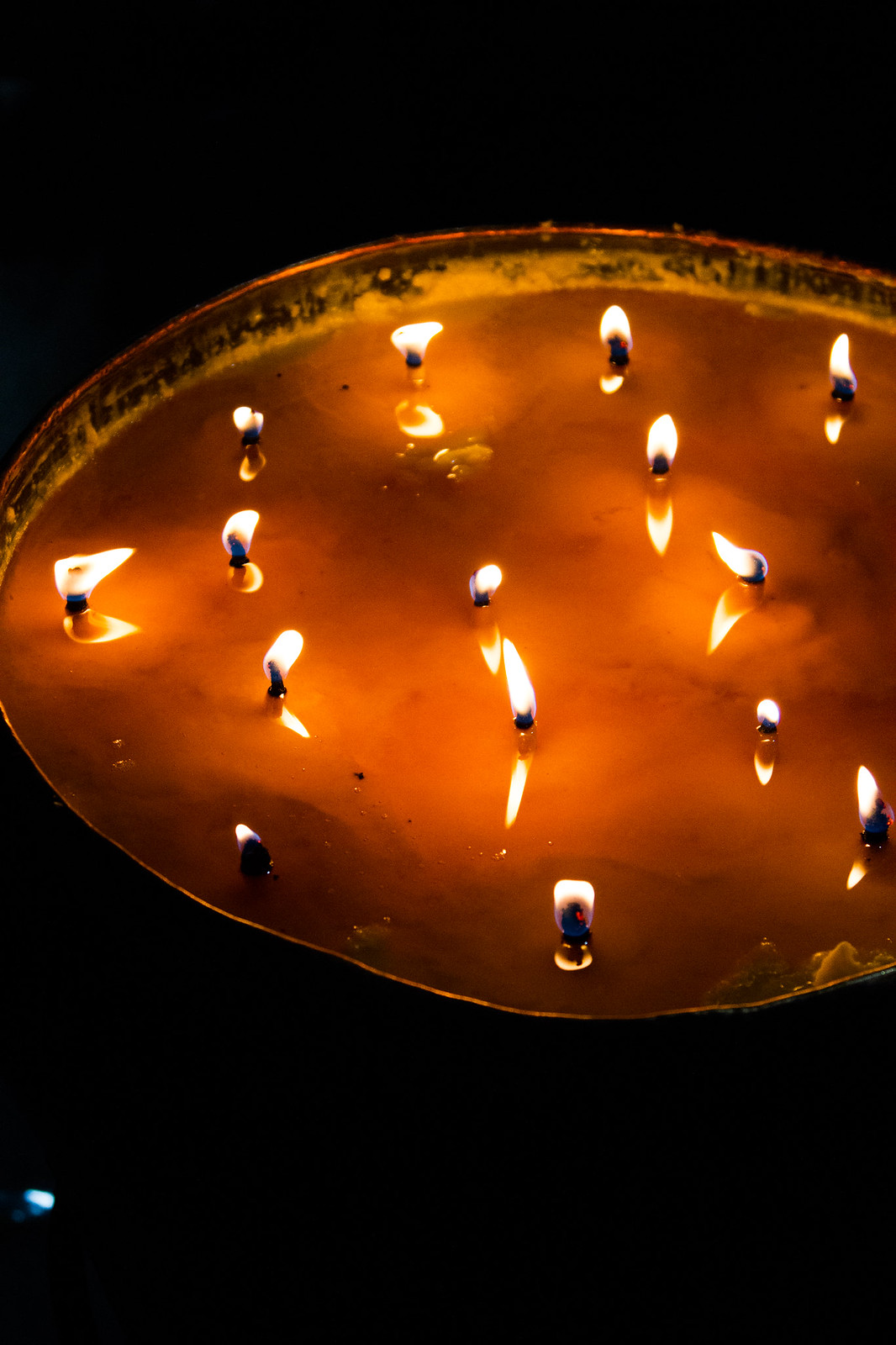 Multiple lit wicks flickering in a large bowl of golden yak butter, glowing against darkness in a Tibetan temple.
