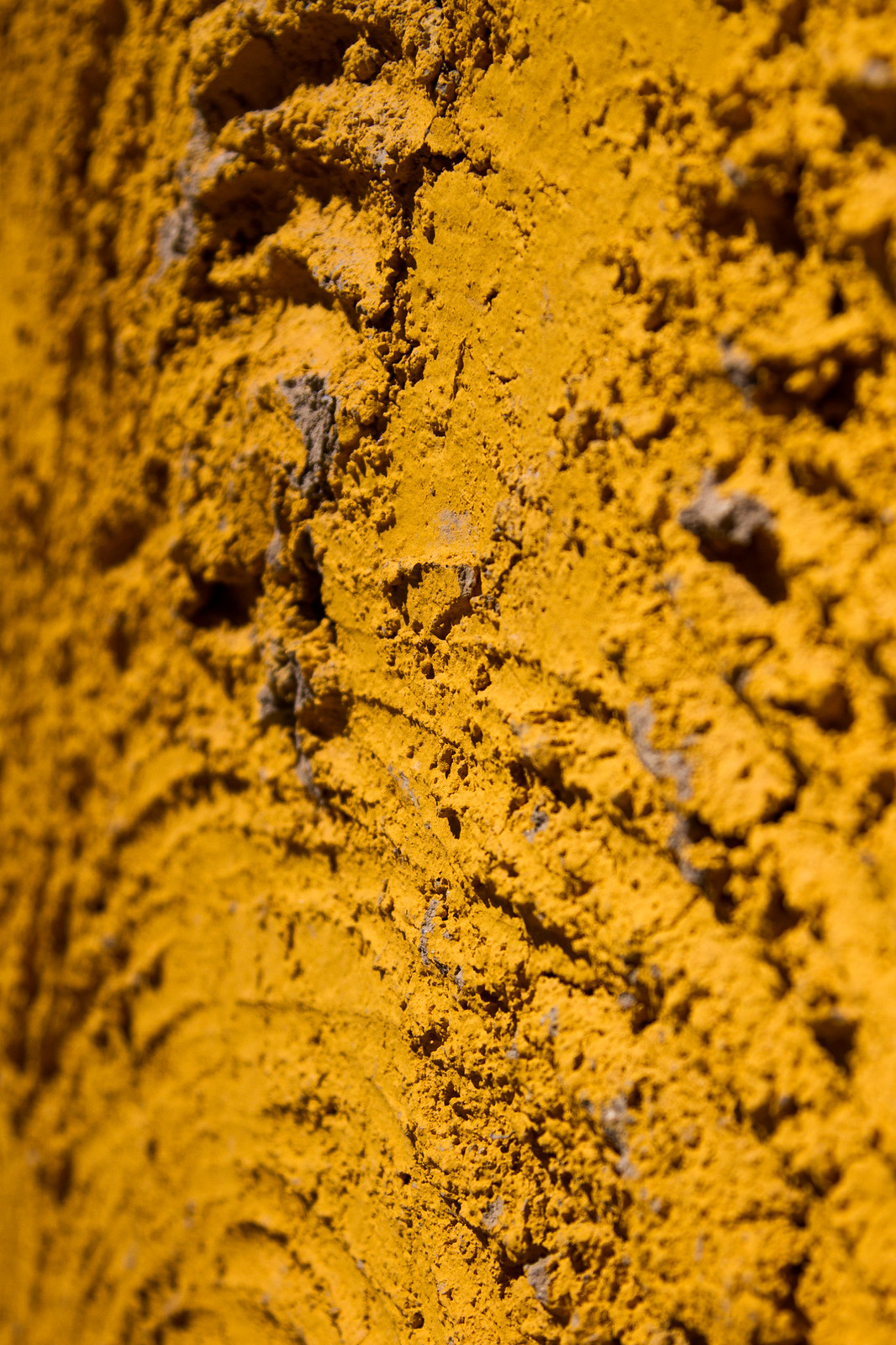 Close-up of a rough, textured wall coated in vivid yellow-ochre pigment with visible tool markings.